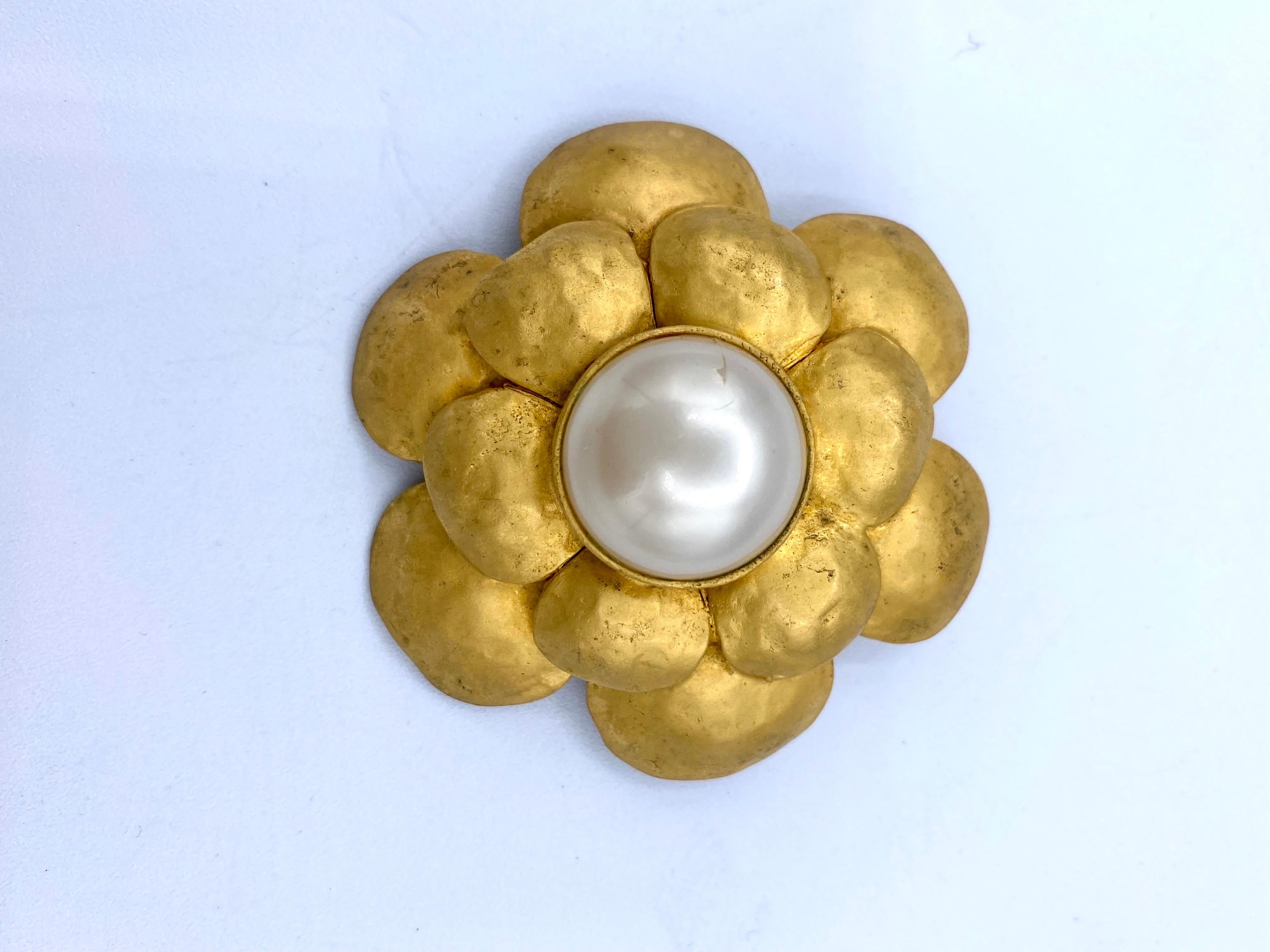 Vintage Chanel Camelia brooch in gold metal centered with a pearly cabochon from 1993.
Width 6cm
height 5.5cm
depth 2.7cm
The central cabochon is 2cm.
The brooch shows traces of use, verdigris on the back and a small mark on the cabochon, all