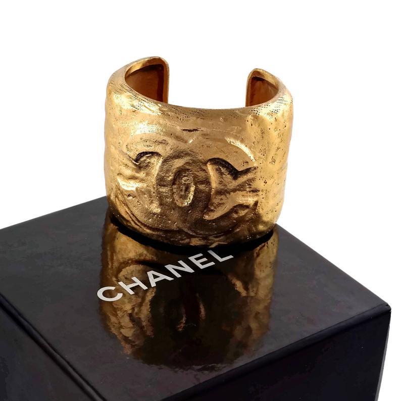 Vintage CHANEL CC Logo Hammered Cuff Bracelet

Measurements:
Height: 2.16 inch (5.5 cm)
Circumference: 6.49 inches (16.5 cm)
Opening:1.18 inches (3 cm)

Features:
- 100% Authentic CHANEL.
- Hammered gilt cuff bracelet with raised CC logo at the