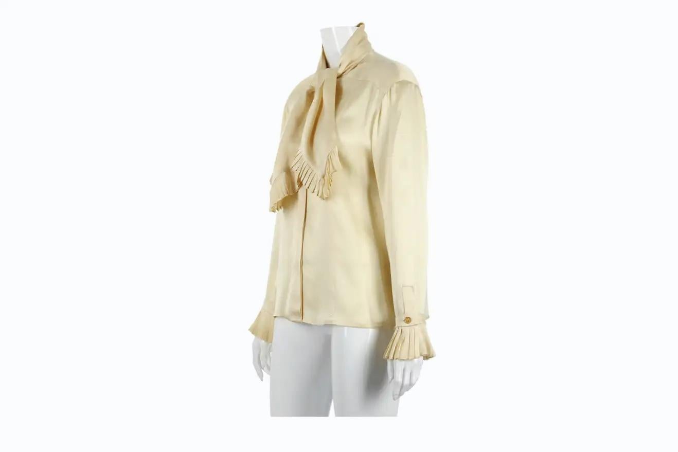 Vintage Chanel cream silk charmeuse blouse with knife pleated trim at the neckties and sleeve cuffs. Features hidden button closures down center front and goldtone CC logo buttons at the cuffs. No size tag - please consult measurements.
