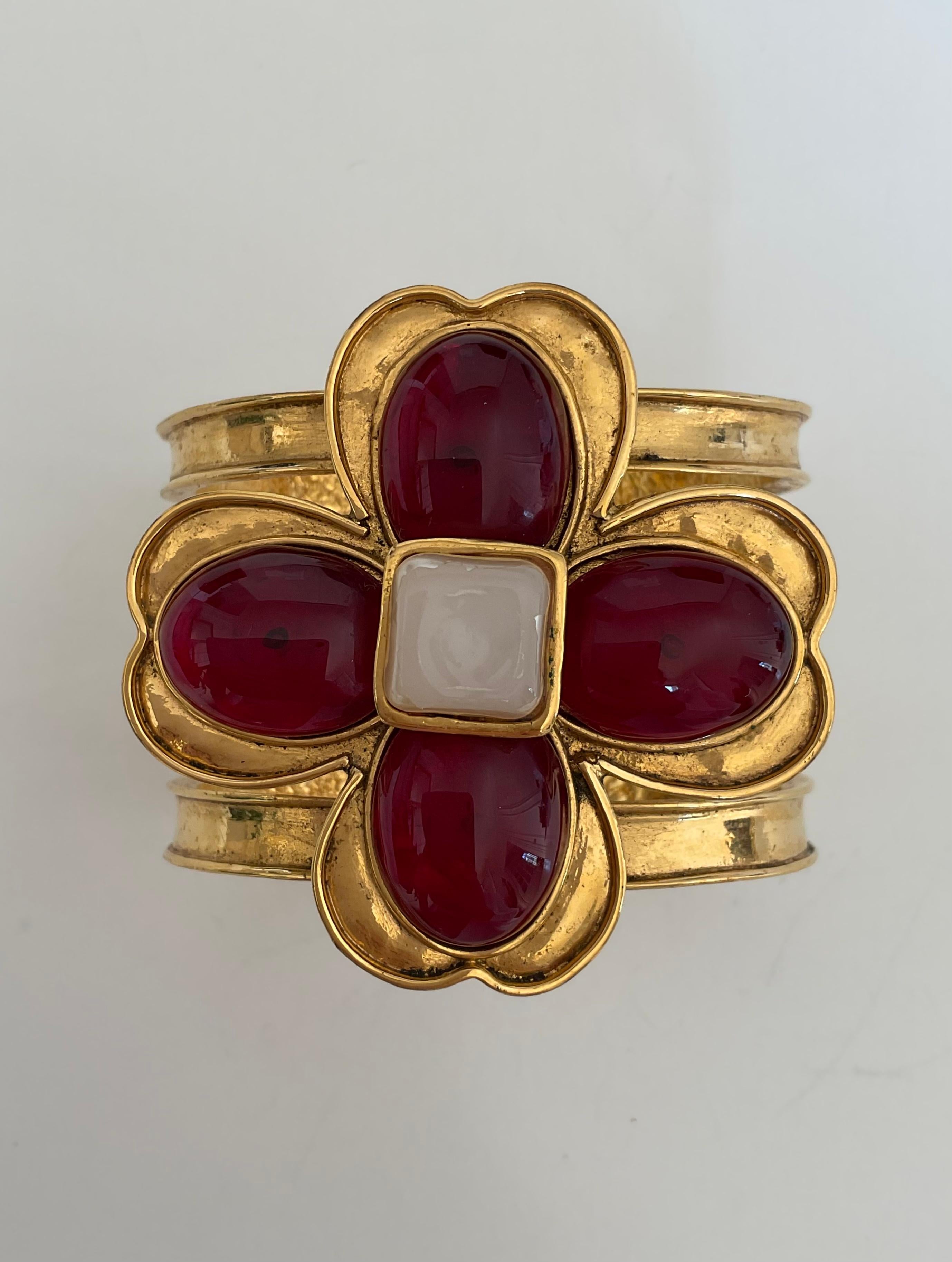 This item is a Vintage CHANEL gold toned cuff. The impressive bracelet is composed of three rows and a flower design at his centre: a faux pearl square-shaped in the centre and four red toned petals in “pate de verre” with gold-plate petals