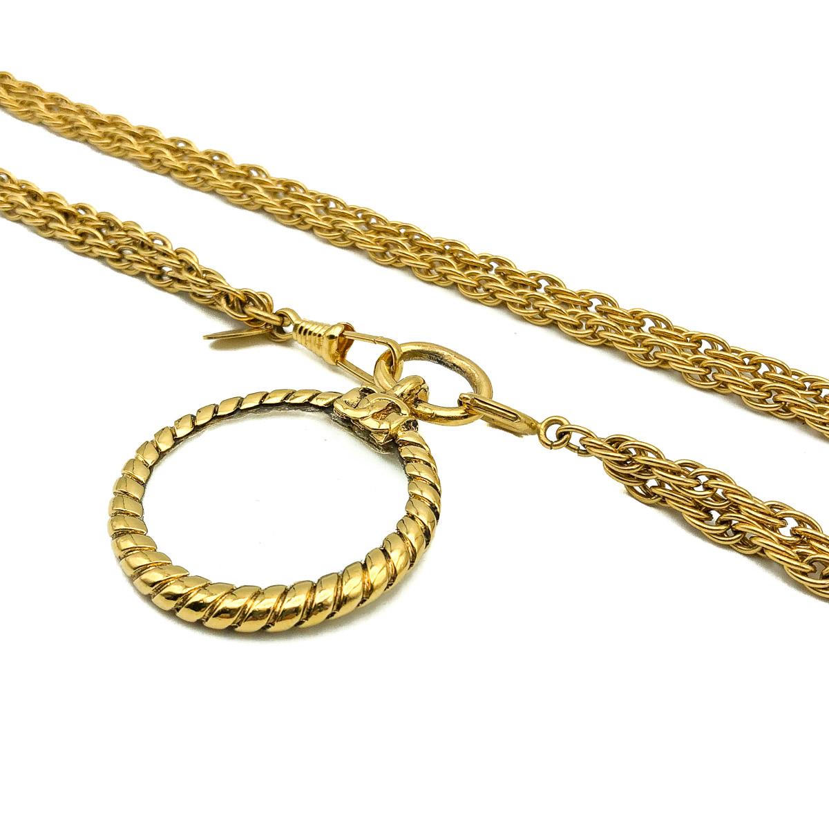 Un superbe collier vintage Chanel en forme de miroir. Réalisée en métal doré et sertie d'une loupe ornée du logo iconique de la maison Chanel, les C emboîtés.  Objet vintage en très bon état. Signé. Chaîne d'environ 94 cm et pendentif de 5,5 cm.
