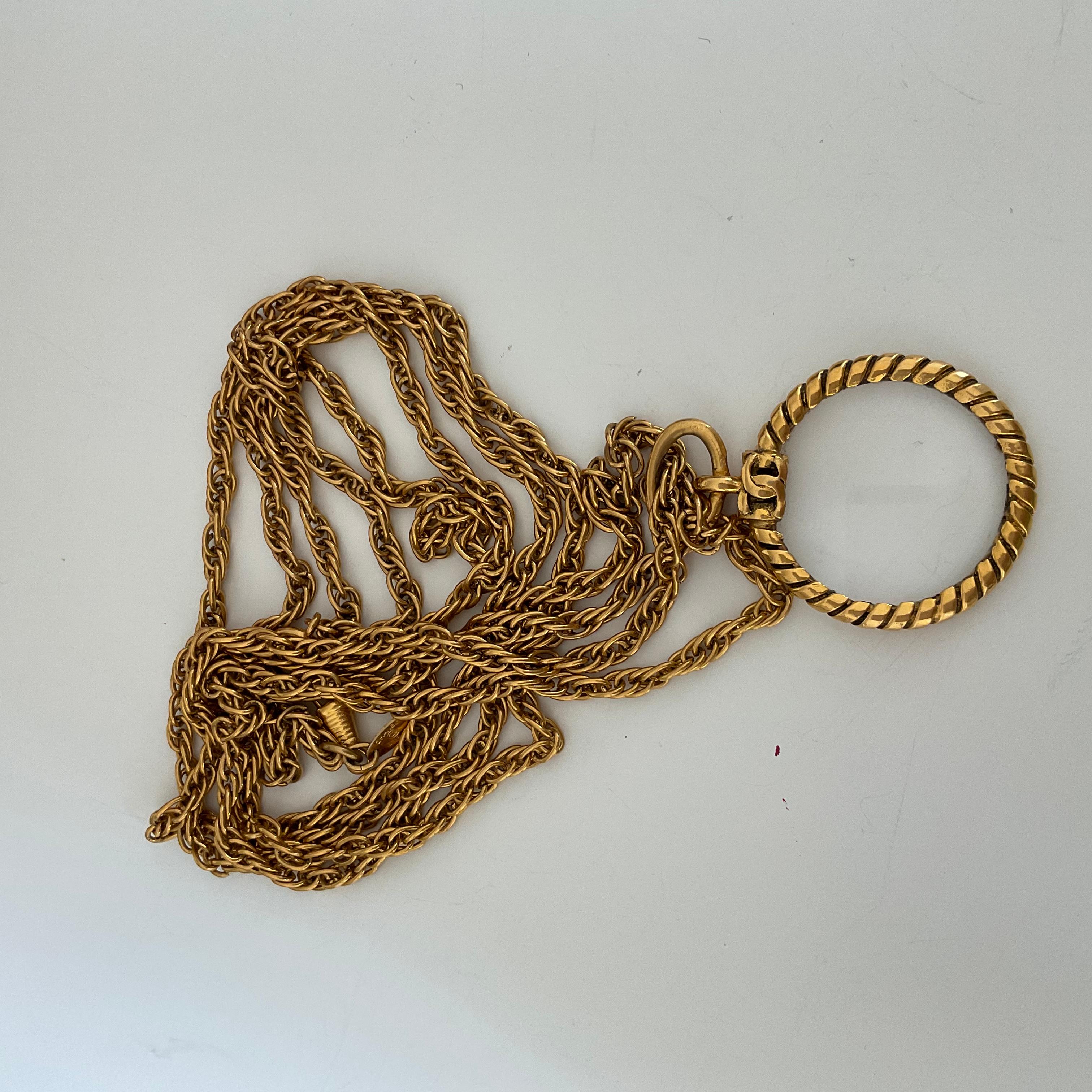 Dieses seltene Stück ist eine vergoldete Vintage CHANEL-Halskette, die aus doppelt gedrehten Ketten besteht. Als Anhänger finden Sie ein Lupenglas, das von einer weiteren Torsade umgeben ist. Auf der Oberseite des Anhängers, wo die Ketten befestigt