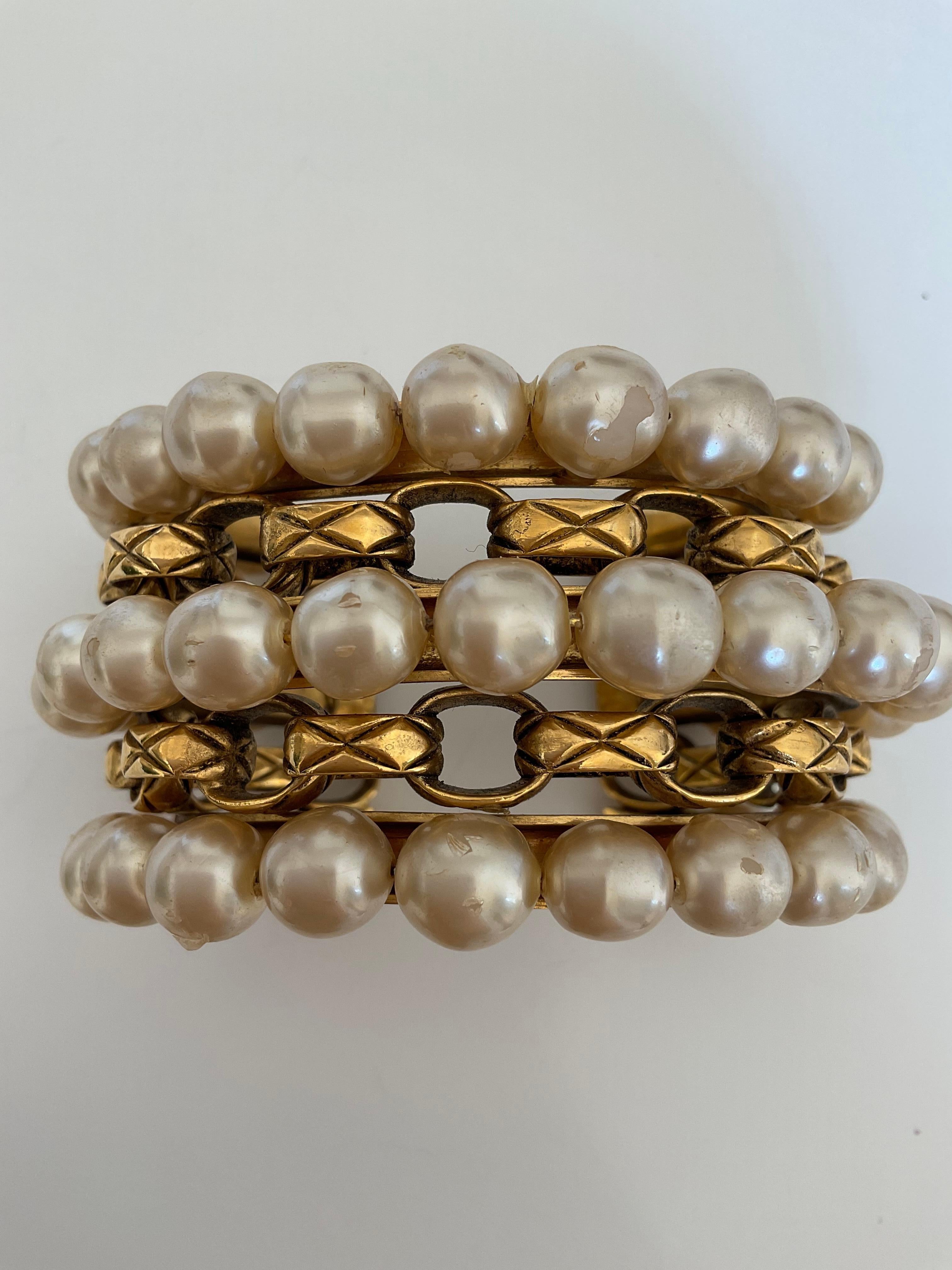 This piece from the 80’s is a Vintage CHANEL cuff made in gold plate. This rare bracelet is composed of three gold rows of faux pearls in resin and two rows of the iconic quilted chain known of the House. The Haute couture cuff is stamped “Chanel 2