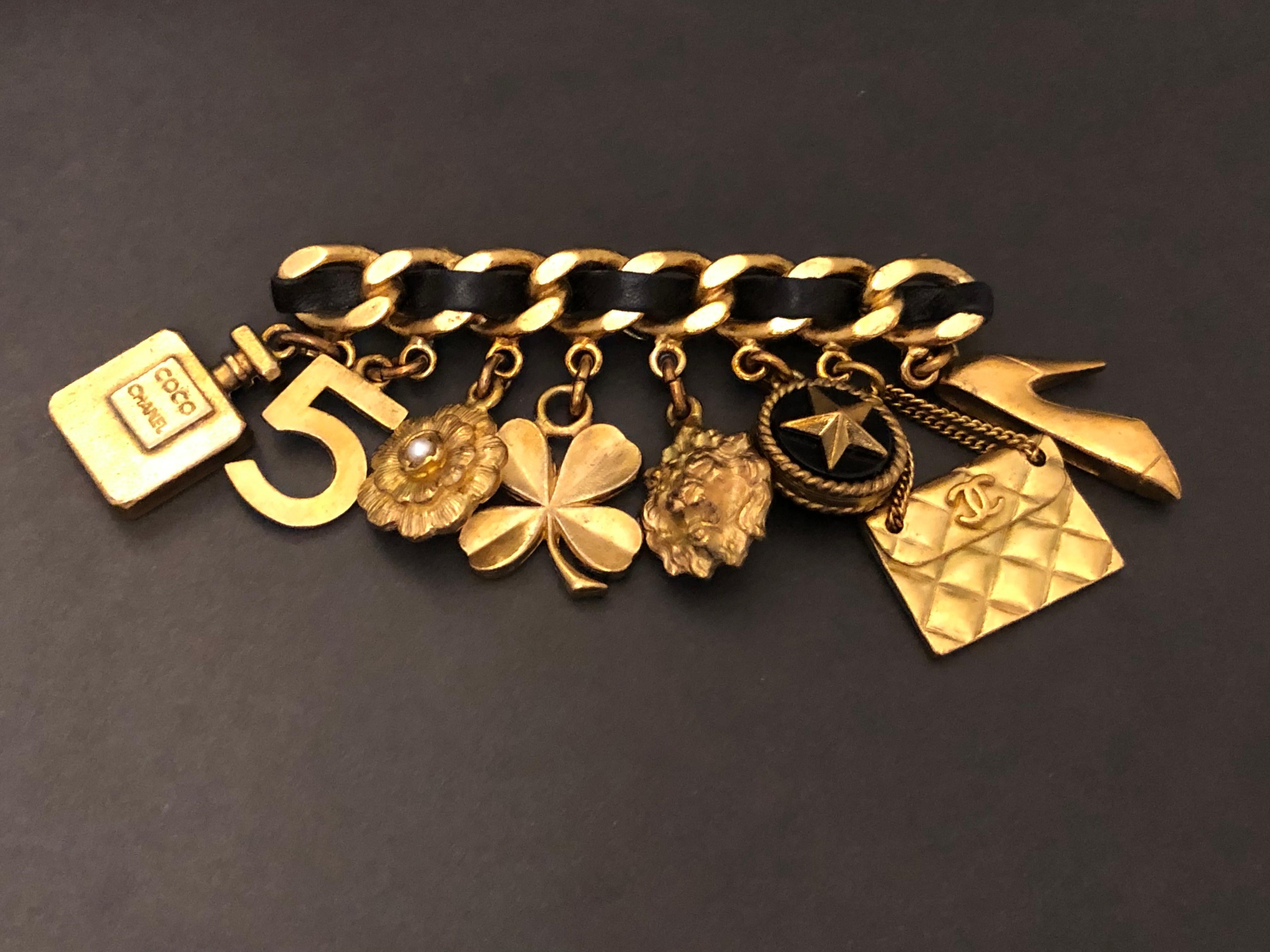 1994 Vintage Chanel gold toned chain brooch featuring eight iconic motifs including clover, camellia, lion, No.5, perfume bottle etc interlaced with black leather.  Stamped 94A made in France. Measures approximately 8.2 x 5.1 cm. Comes with box.