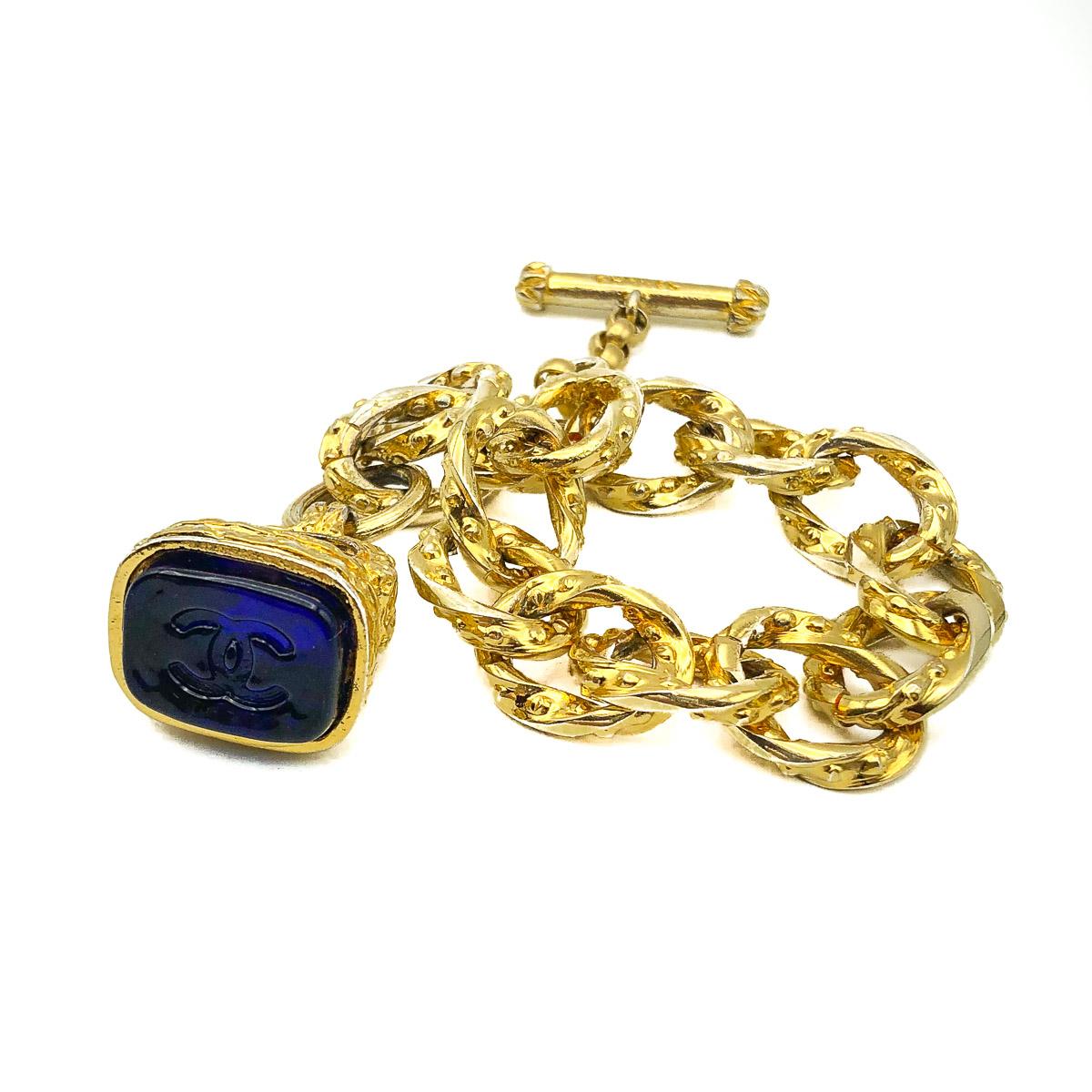A fabulous Vintage Chanel Gripoix Bracelet originating from the 90s heyday of Lagerfeld and Victoire de Castellane. Featuring large open chased gold plated links with an ornate wax seal style fob set with a large blue pate de verre CC logo stone.
