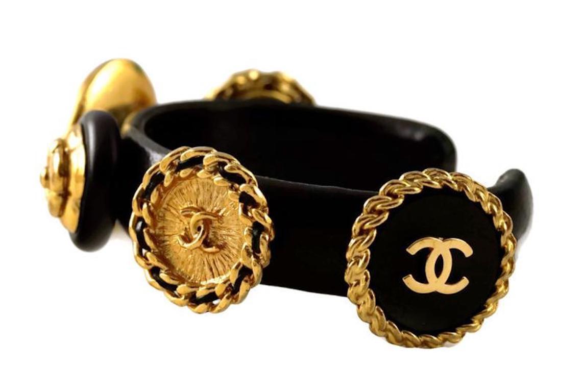 Vintage CHANEL Iconic Logo Lamb Skin Leather Cuff Bracelet

Measurements:
Height: 1 inch (largest button)
Inside Diameter: 2 1/8 inches
Opening: 1 inch

Features:
- 100% Authentic CHANEL.
- Black lamb skin leather cuff.
- Accentuated with 6 iconic