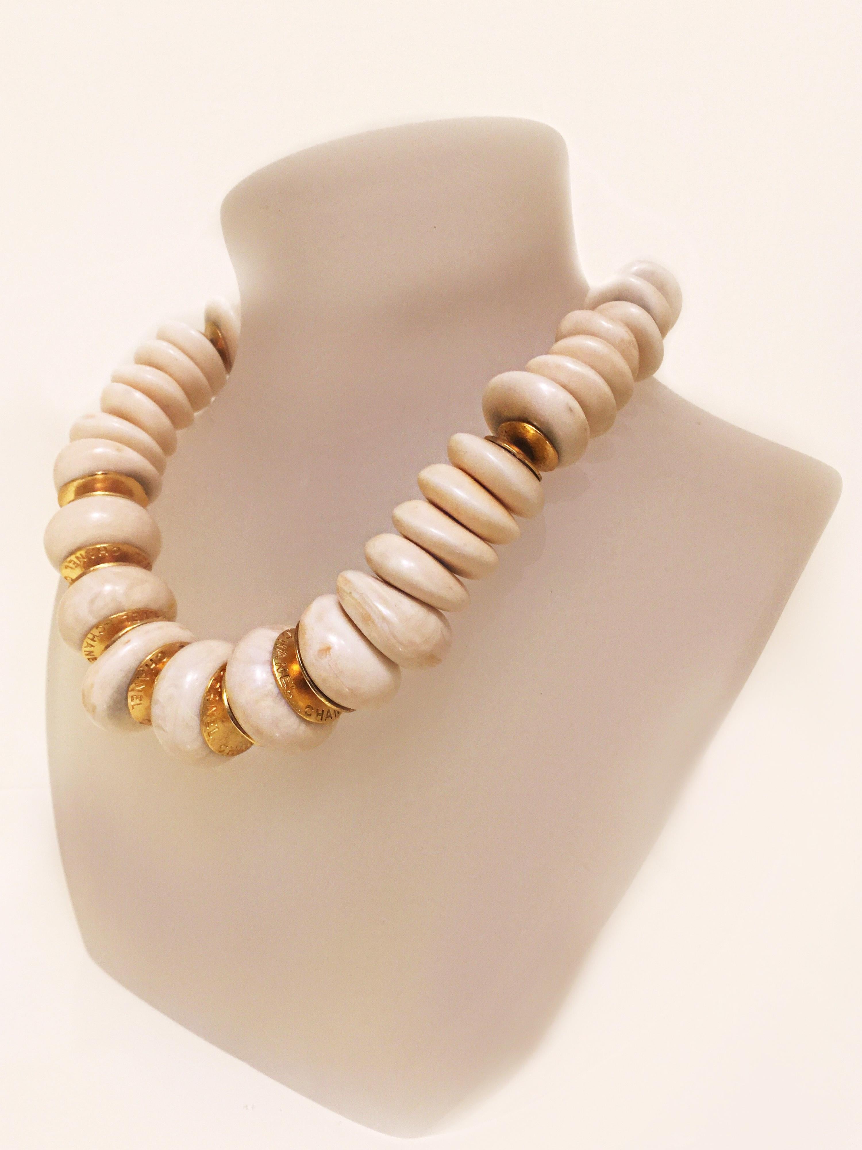 From the 90's era this rare Chanel necklace is a knockout. The large, ivory marbleized beads of resin, are intertwined with gold disc accents;  each one is engraved Chanel. Interlocking CC engraved gold beads at the back with adjustable hook and