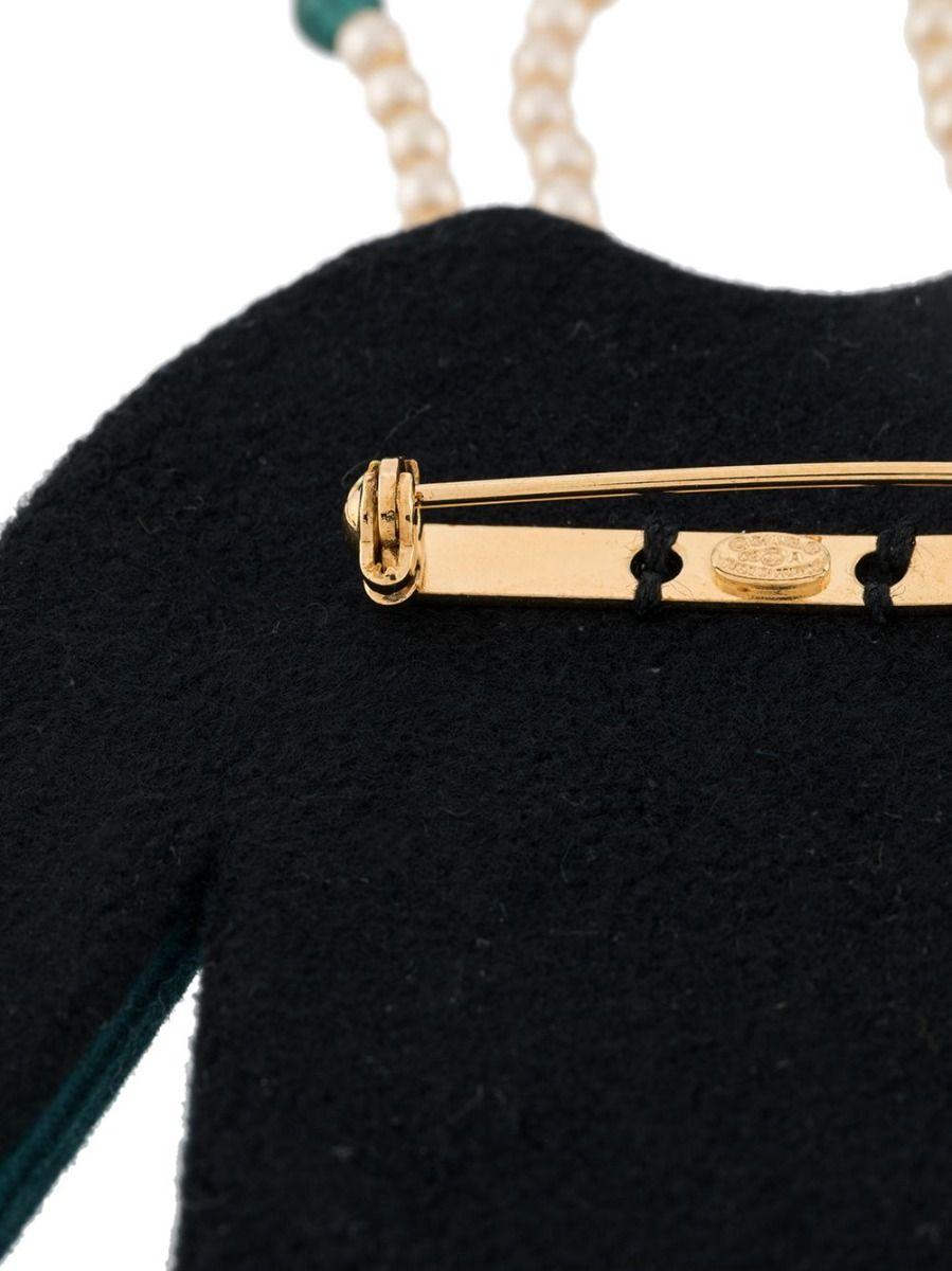 This rare vintage brooch from Chanel is styled after the house's signature jacket. It features the monogram detailing on the pockets, faux-pearl button embellishments, along with a faux-pearl double strand necklace.

Colour: Peacock blue

Material: