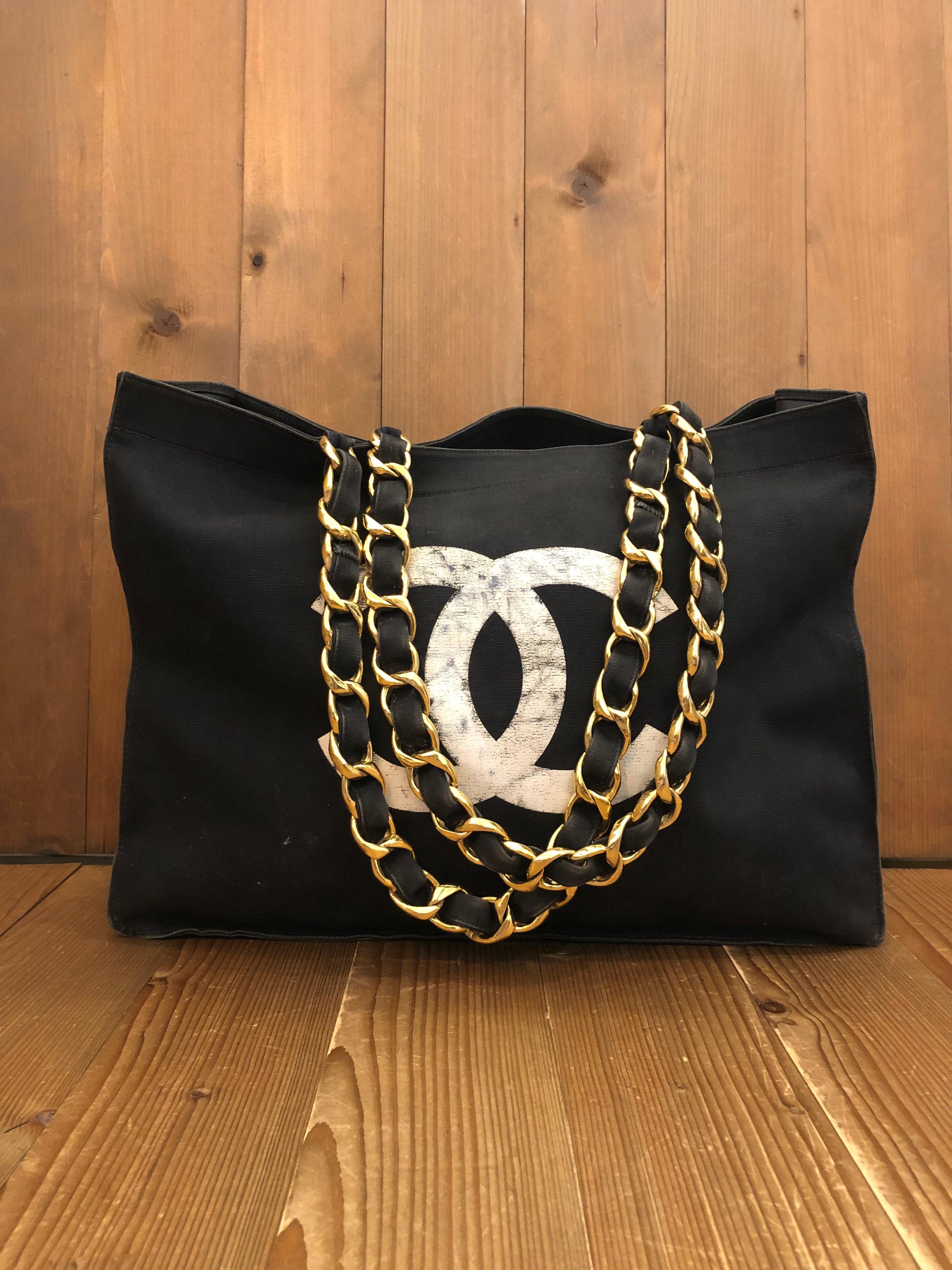 This vintage CHANEL jumbo chain tote is crafted of black canvas featuring a massive screen printed CC logo and “CHANEL” letters. This tote has two sturdy gold toned shoulder chains interlaced with black canvas that opens to a coated interior in