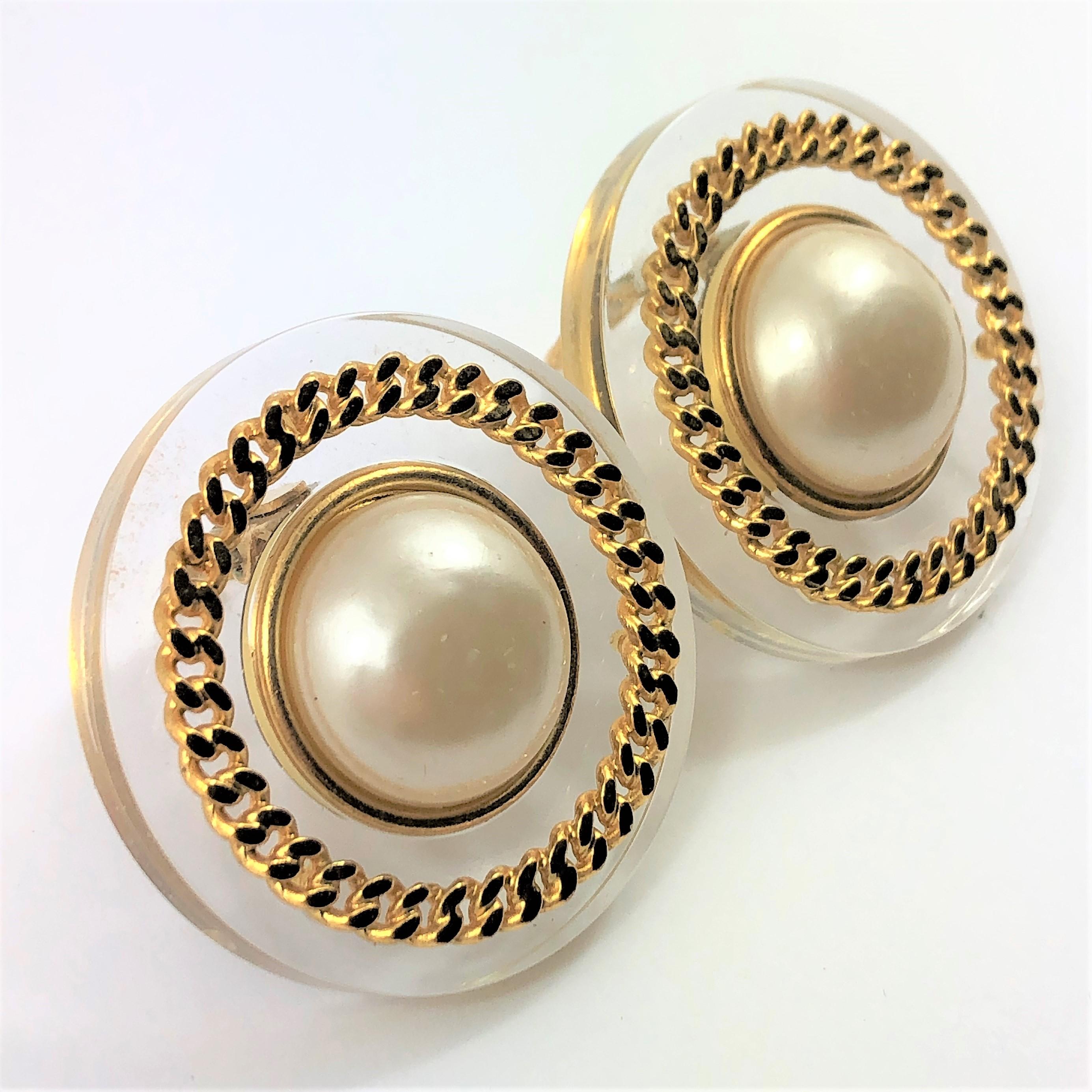 Measuring 1 5/8 inch across, these jumbo size Chanel earrings are fabulous for any season. The clear plexiglass, with the large faux pearls and gold tone chain accents are as stylish
today as they were when they were manufactured as part of Chanel's