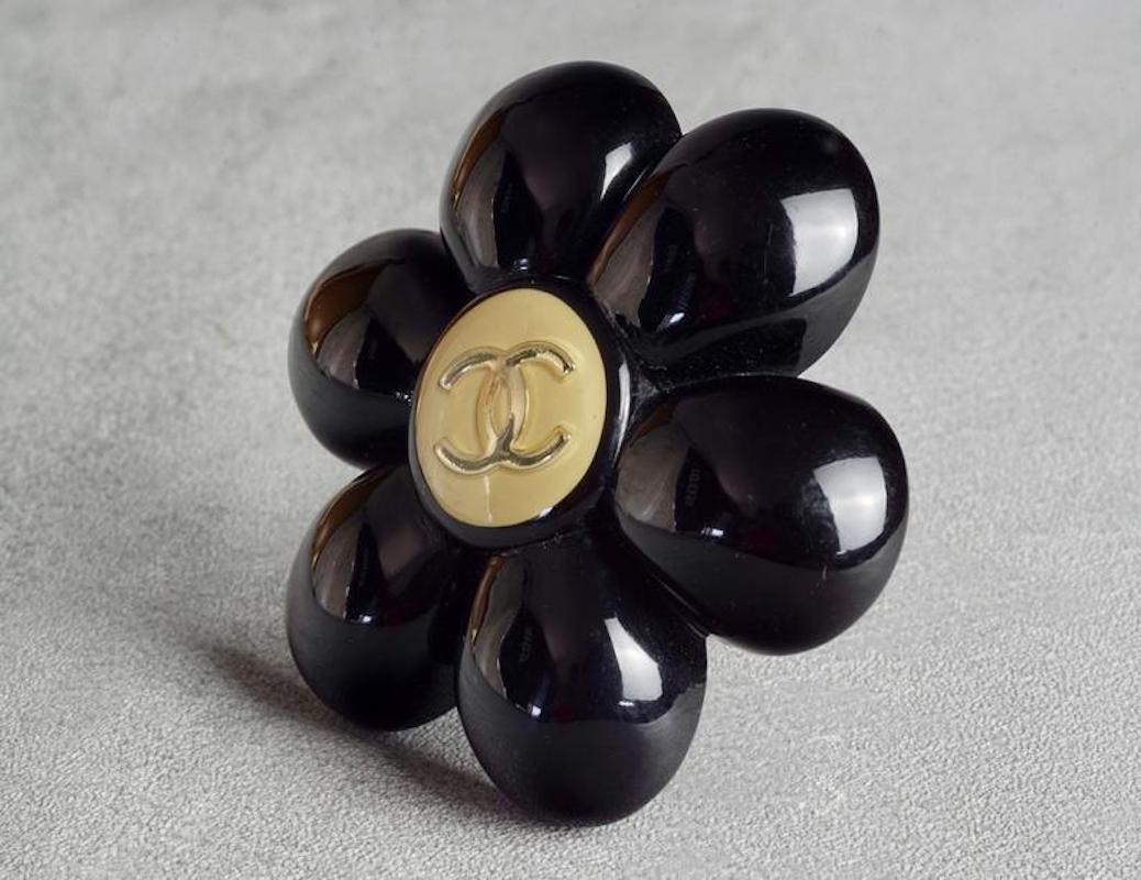 Vintage CHANEL Logo Black Camellia Resin Brooch

Measurements:
Height: 2.16 inches (5.5 cm)
Width: 2.16 inches (5.5 cm)

Features:
- 100% Authentic CHANEL.
- Black resin camellia flower with CC logo at the centre.
- Silver tone hardware.
- Signed