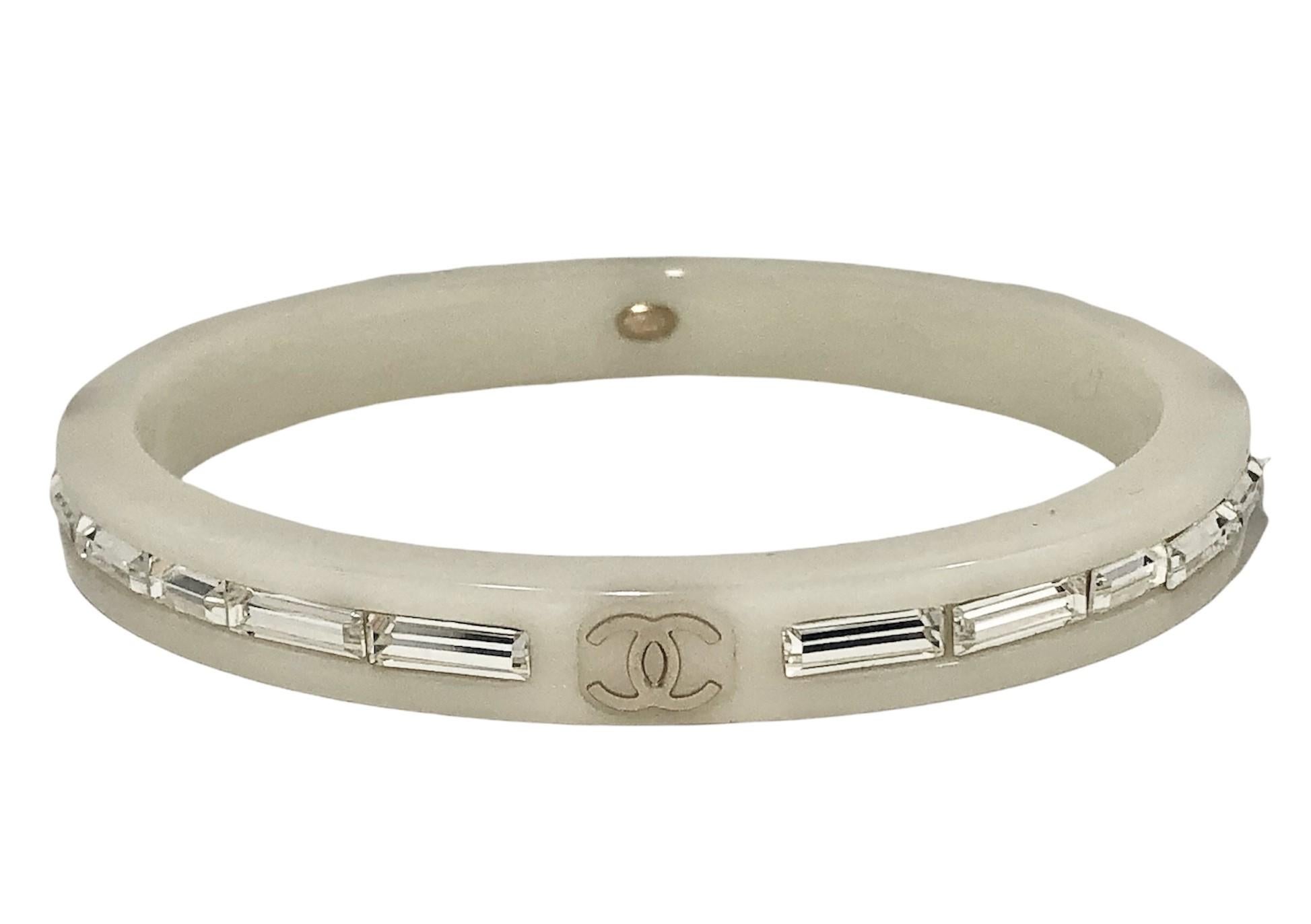 This stylish Chanel bangle bracelet is crafted in white resin embedded with baguette crystals all around. The continuous line is punctuated at four positions by the familiar  