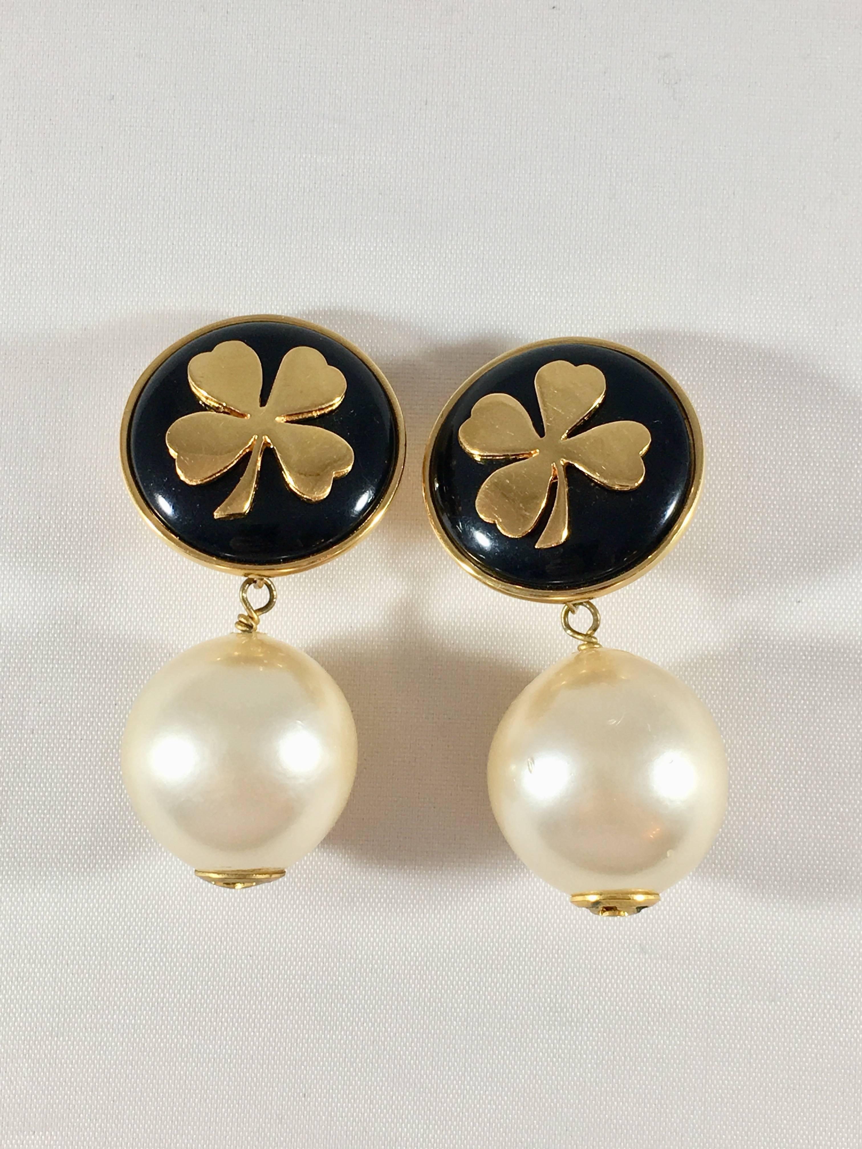 These are a fabulous pair of 1970s Chanel earrings featuring a large round faux pearl hanging from a piece embellished with a gold clover set in a black resin background. The clover is a symbol that was often used by Chanel. It was one of the
