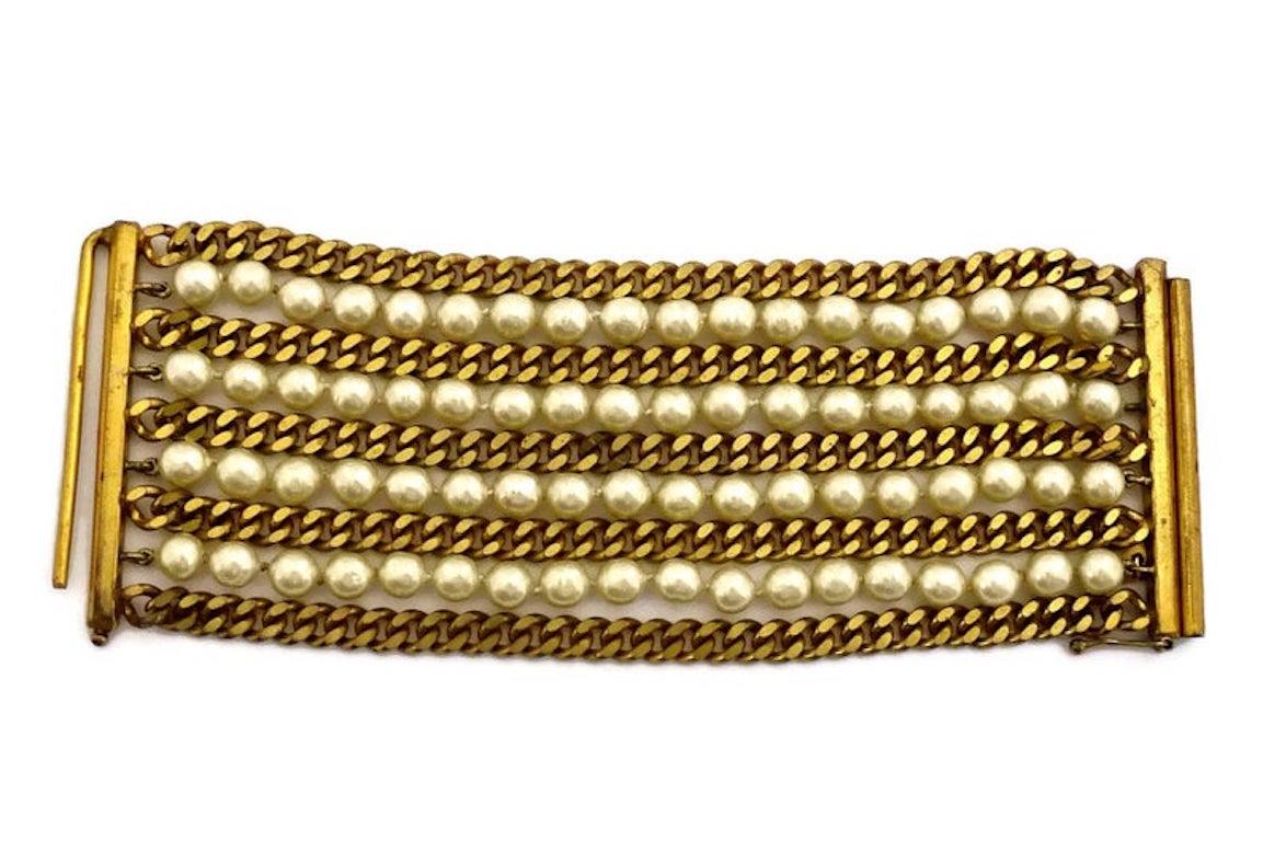 Vintage CHANEL Pearl Chain 9 Multistrand Wide Bracelet

Measurements:
Height: 2.75 inches (7 cm)
Length: 7 inches (18 cm)

Features:
- 100% Authentic CHANEL.
- 9 Multistrand chain and glass pearl wide bracelet.
- Gold tone.
- Signed CHANEL CC Made