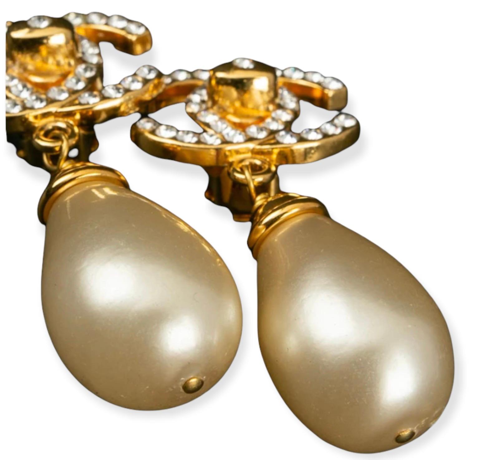 Chanel  Clip on gilded metal earrings comprised of a cc logo paved with rhinestones, from which dangles a pearly drop . 1996 Fall-Winter Collection.