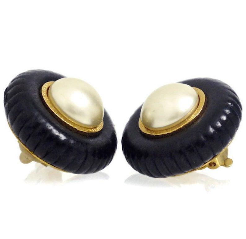 Vintage Chanel Pearl Leather Tyre Rim Earrings

Measurements:
Height: 1 2/8 inches
Width: 1 6/8 inches
Depth: 6/8 inch

Features:
- 100% Authentic CHANEL.
- Black leather in the form of a tyre.
- Faux pearl at the centre.
- Gold tone hardware.
-