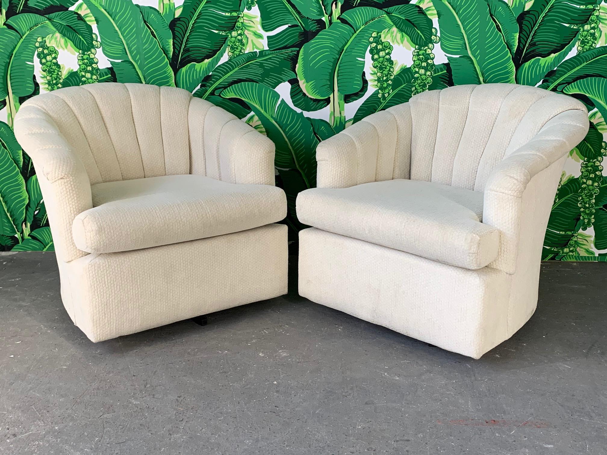 Pair of swivel club chairs featuring channel back upholstery in a textured white fabric. Very comfortable and in good condition with minor imperfections consistent with age (see photos). Perfect addition to your Hollywood Regency decor.
   
    