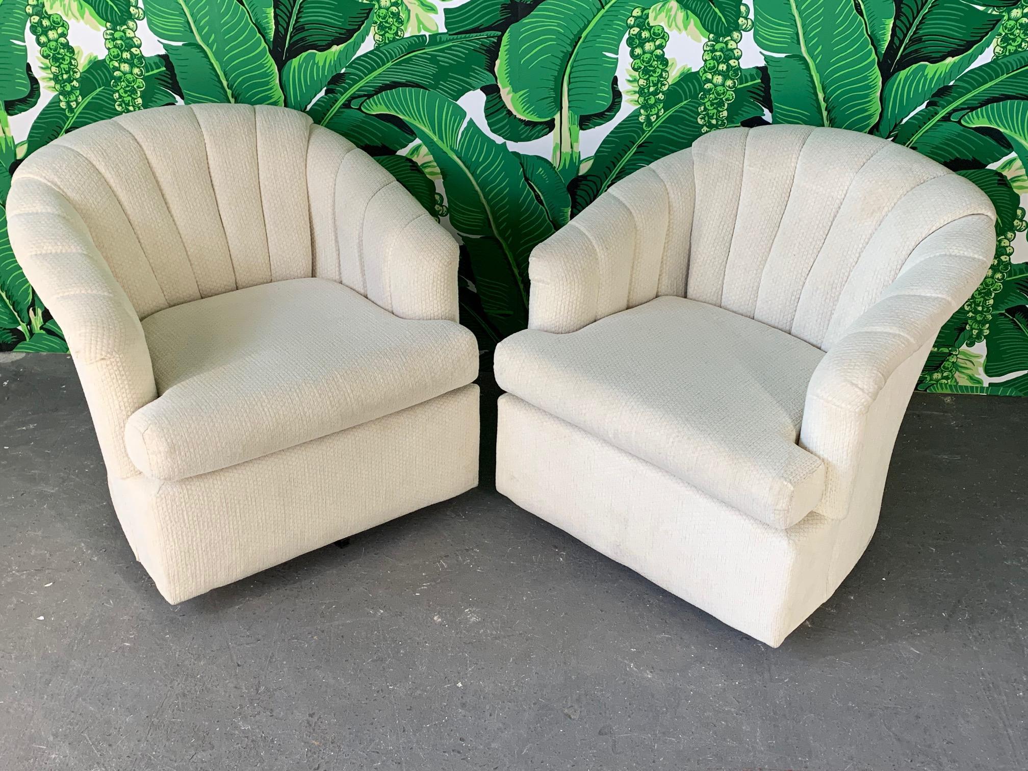 Pair of swivel club chairs featuring channel back upholstery in a textured white fabric. Very comfortable and in good condition with minor imperfections consistent with age (see photos). Perfect addition to your Hollywood Regency decor.