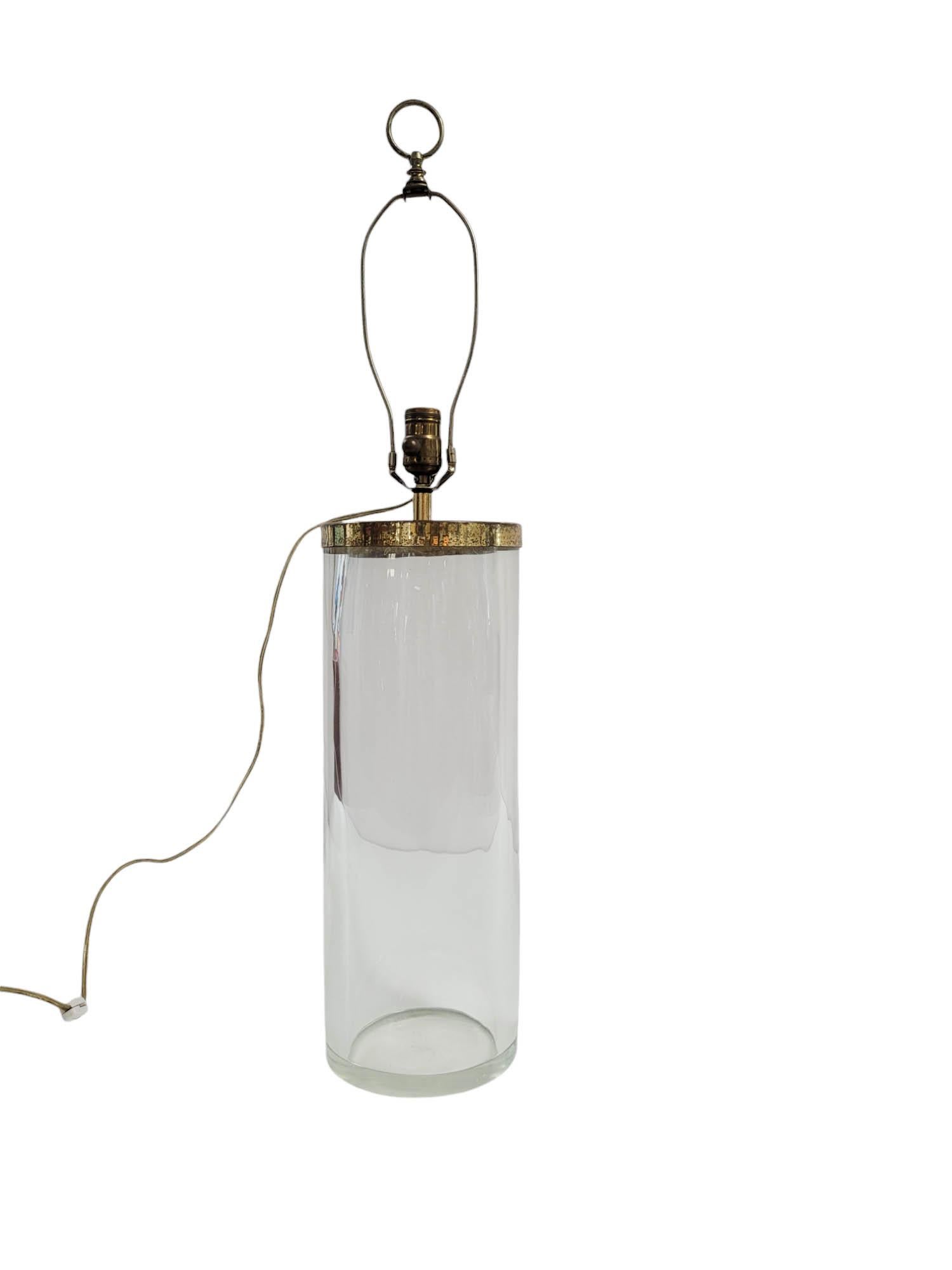 Crafted by Chapman Manufacturing in the 1970s, this vintage table lamp features a clear cylindrical body made of thick 1/4-inch glass, paired with a solid brass neck and socket assembly. A unique design detail—the power cord emerging just below the