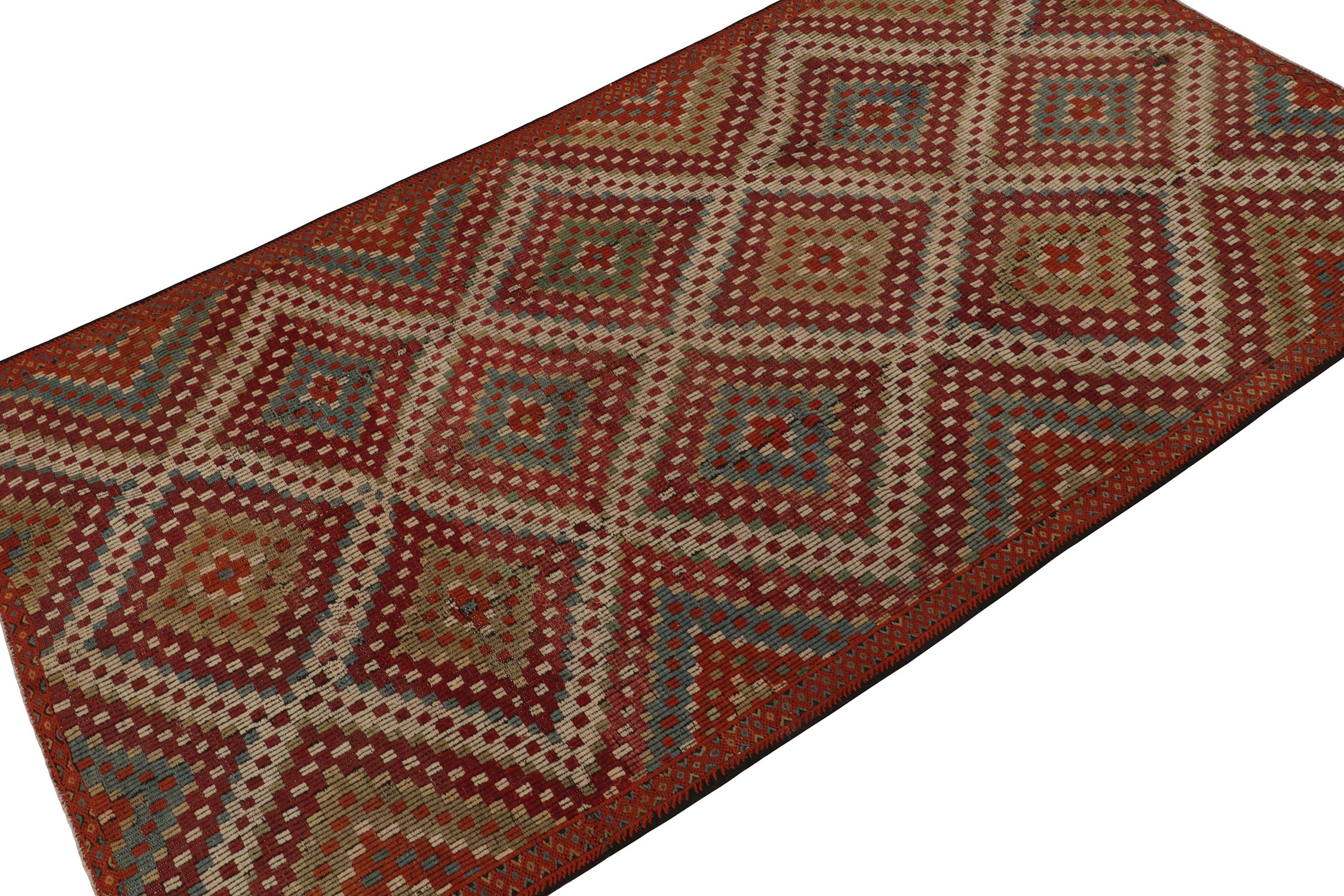 Originating from Turkey circa 1950-1960, a vintage Chaput style kilim rug connoting elaborate tribal sensibilities. Handwoven in wool, the piece exhibits a play of blue and green atop a red background with elaborate traditional diamond patterns.