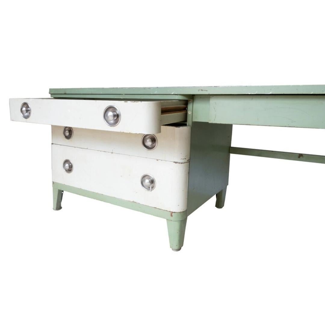 Esempio intramontabile di design Art Déco, questa scrivania sfoggia l'iconica tavolozza verde e crema dell'epoca, completa di bordi graziosamente curvi e di tiretti in metallo lucido. L'usura è coerente con l'età e l'uso. Vedi le foto per i