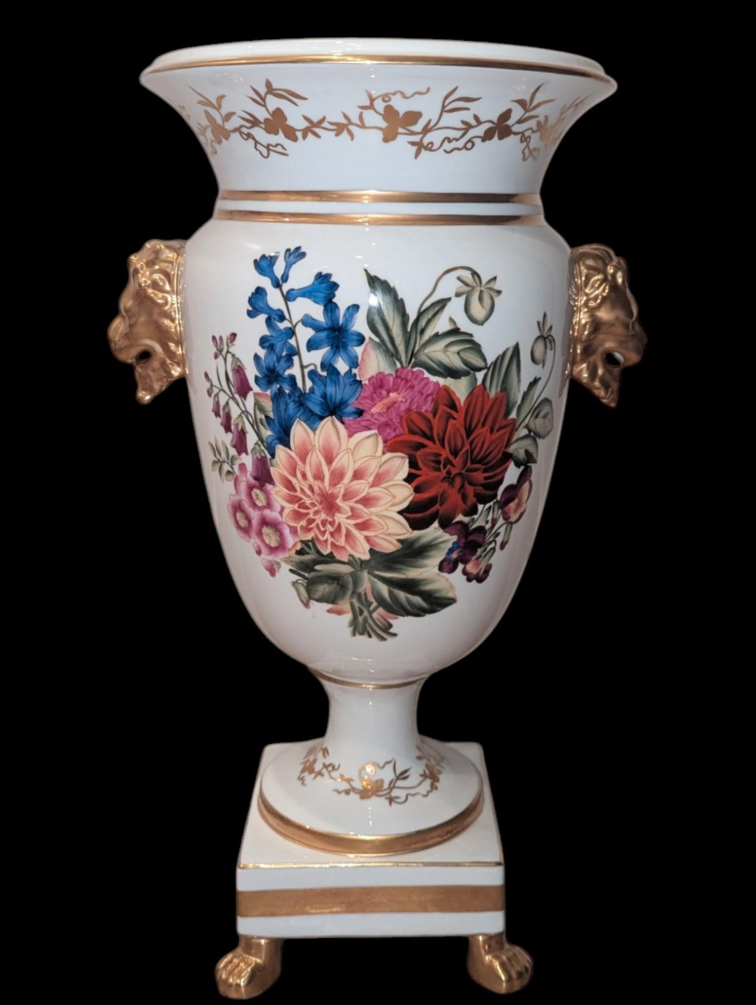 This stunning Vintage Chelsea House Floral Gold Gilt Lion Handle Vase is a beautiful example of timeless craftsmanship and sophisticated design. Featuring a classic urn shape, this vase is adorned with intricate hand-painted floral motifs that bring