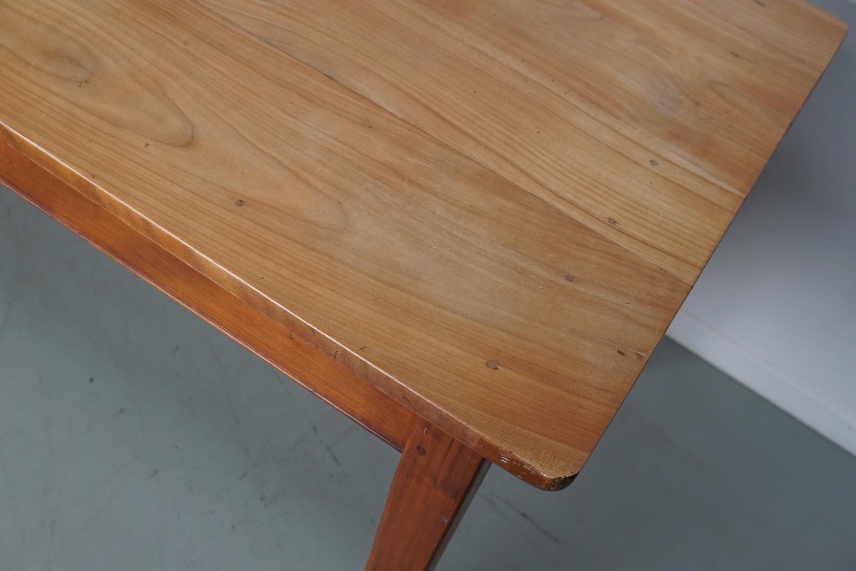Cette élégante table a été fabriquée en France au début/milieu du 20e siècle. Le plateau de la table est en cerisier avec de magnifiques veinures. Sa couleur est très chaude mais claire et la table présente de nombreuses marques d'utilisation et une
