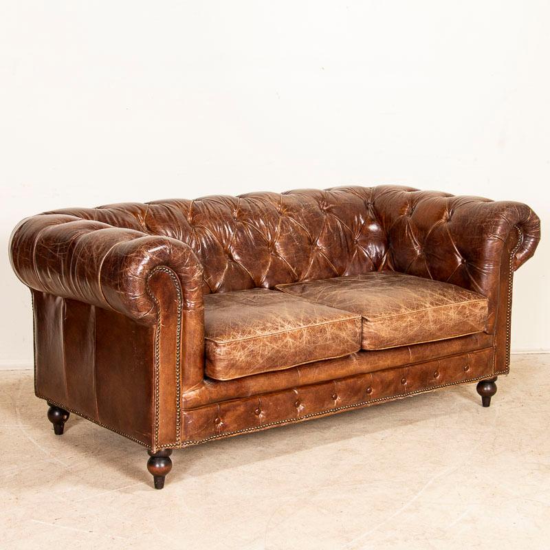 Vintage leather furniture is highly sought after these days, making this loveseat or 2-seat sofa a great find. The tufted Chesterfield back with heavy rolled arms is classic and inviting. The brown leather is in very good condition, all buttons are