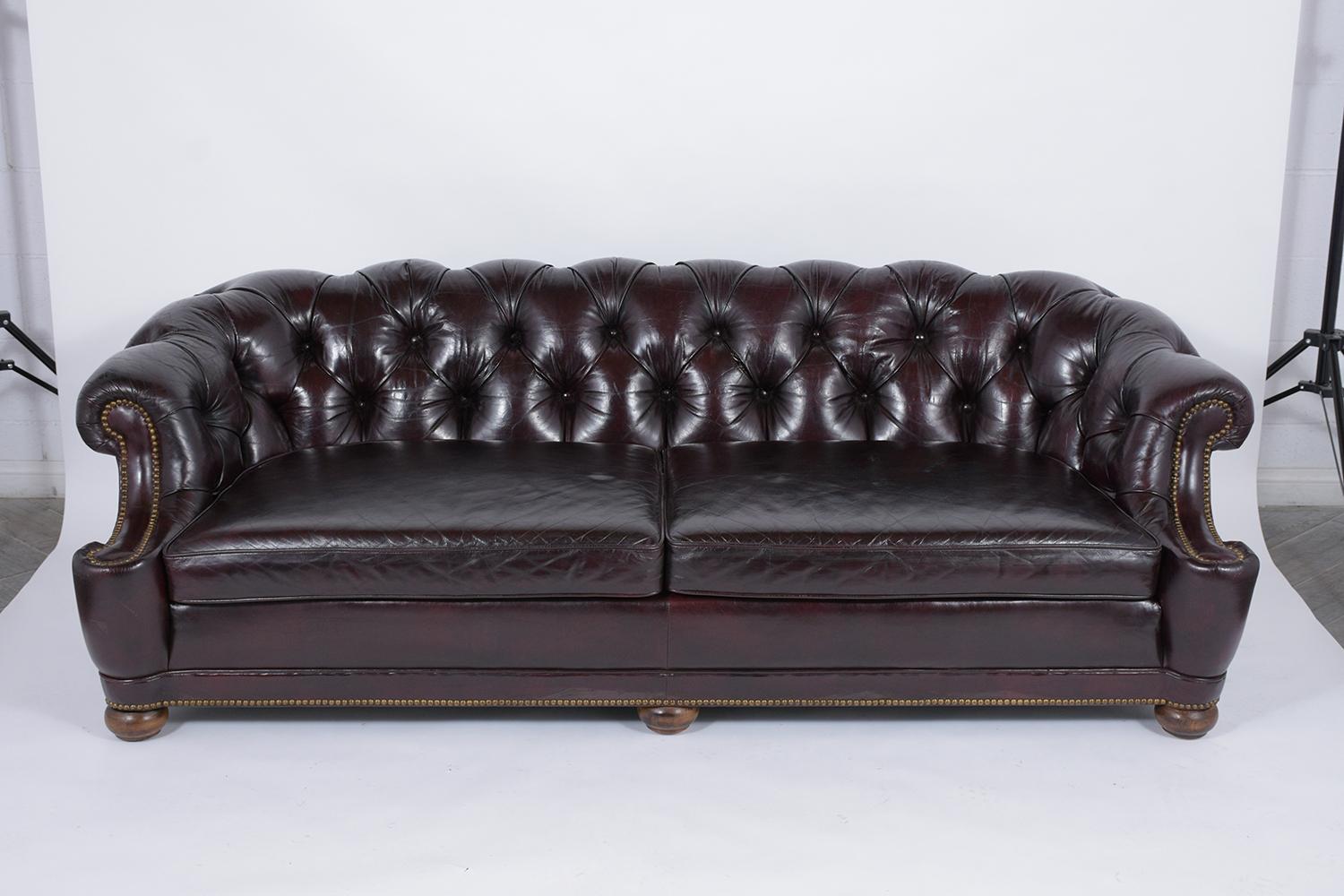 A vintage chesterfield style sofa has been newly refurbished, is crafted out of solid wood and leather, and has been newly dyed in a dark burgundy color and professionally restored by our team of expert craftsmen. The sofa has been waxed giving it a