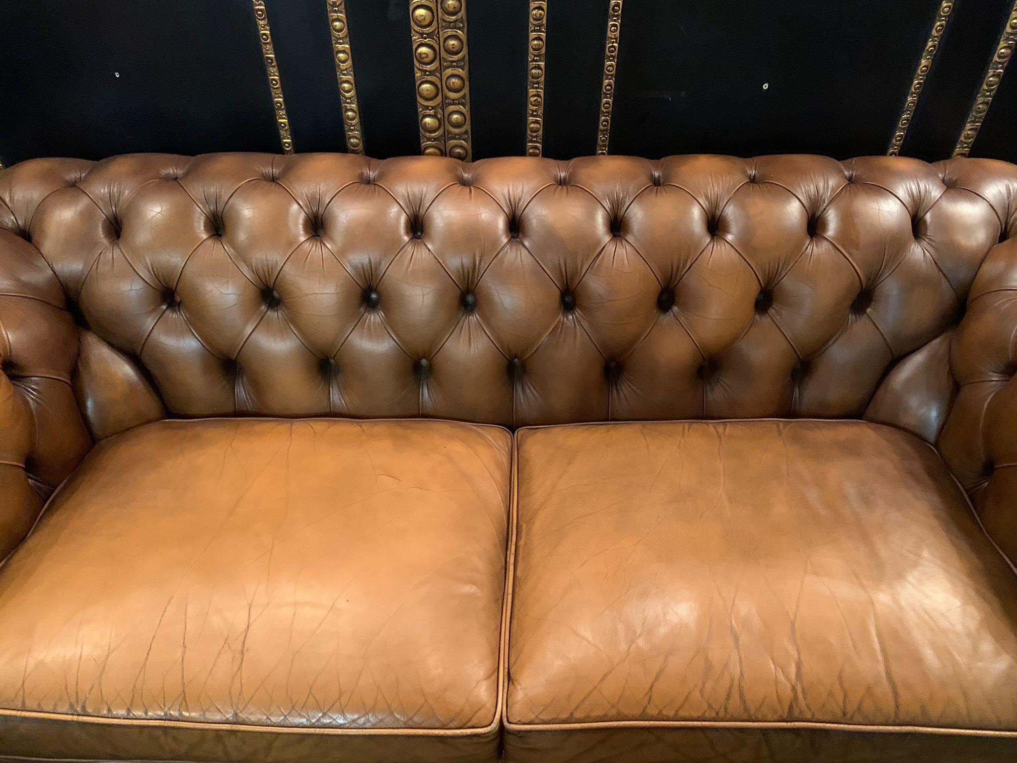 A vintage chesterfield sofa, is crafted out of solid wood and leather, The sofa has been waxed giving it a beautiful patina finish, features a tufted back and arm design, and has a comfortable large seat cushions. 
Leather feet in a rich walnut