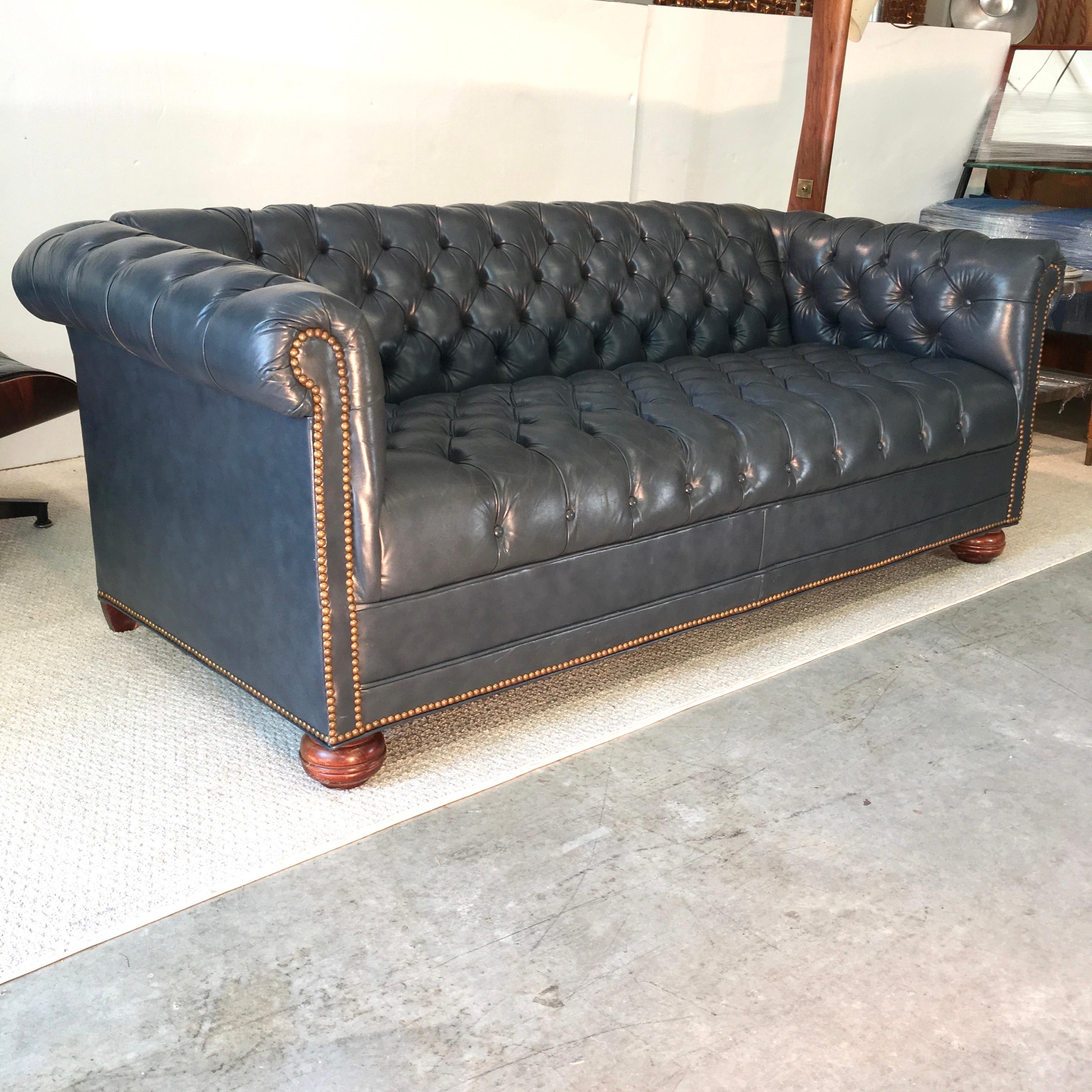 1970s vintage chesterfield sofa in tufted high grade slate blue/gray leather and brass nailhead trim and a fixed tufted seat base. Sits on solid wood bun feet in front and tapered block in the rear. 21 inch seat depth. Very clean and ready to