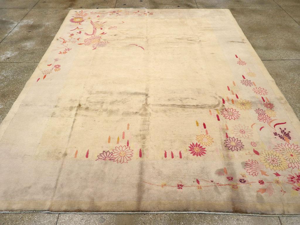 Esta alfombra Art Déco china de mediados del siglo XX, que mide 2,8 m x 3,8 m, presenta un diseño elegante y sobrio con delicados motivos florales dispuestos con gracia sobre el campo. El suave fondo marfil está adornado con un motivo asimétrico de