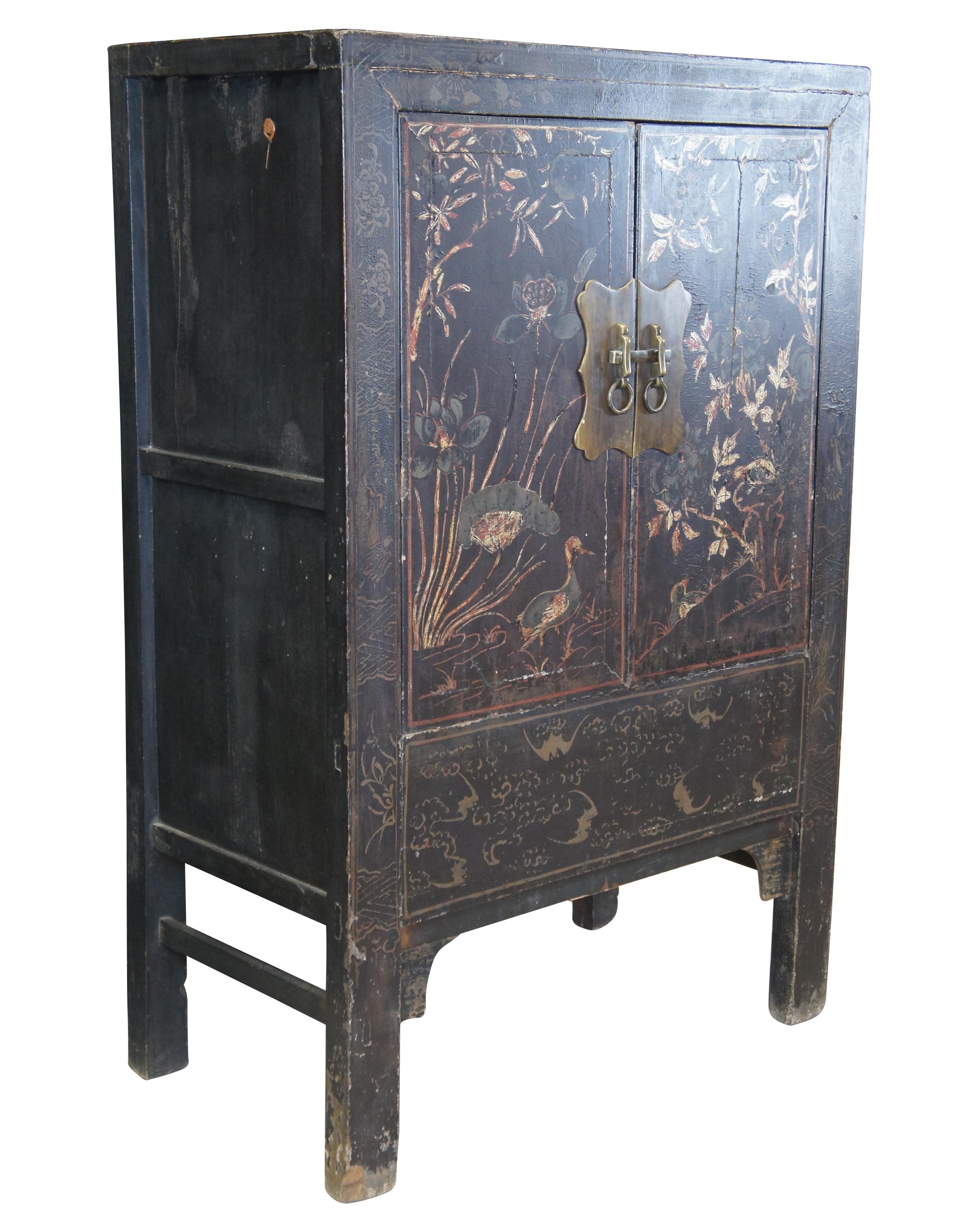 A quaint 20th century chinoiserie Ming style lacquered wardrobe / tv cabinet. Features a beautiful hand painted scene along the front with two ducks amidst a flowery meadow. The hardware is brass with knocker pulls. Interior has two shelves. A