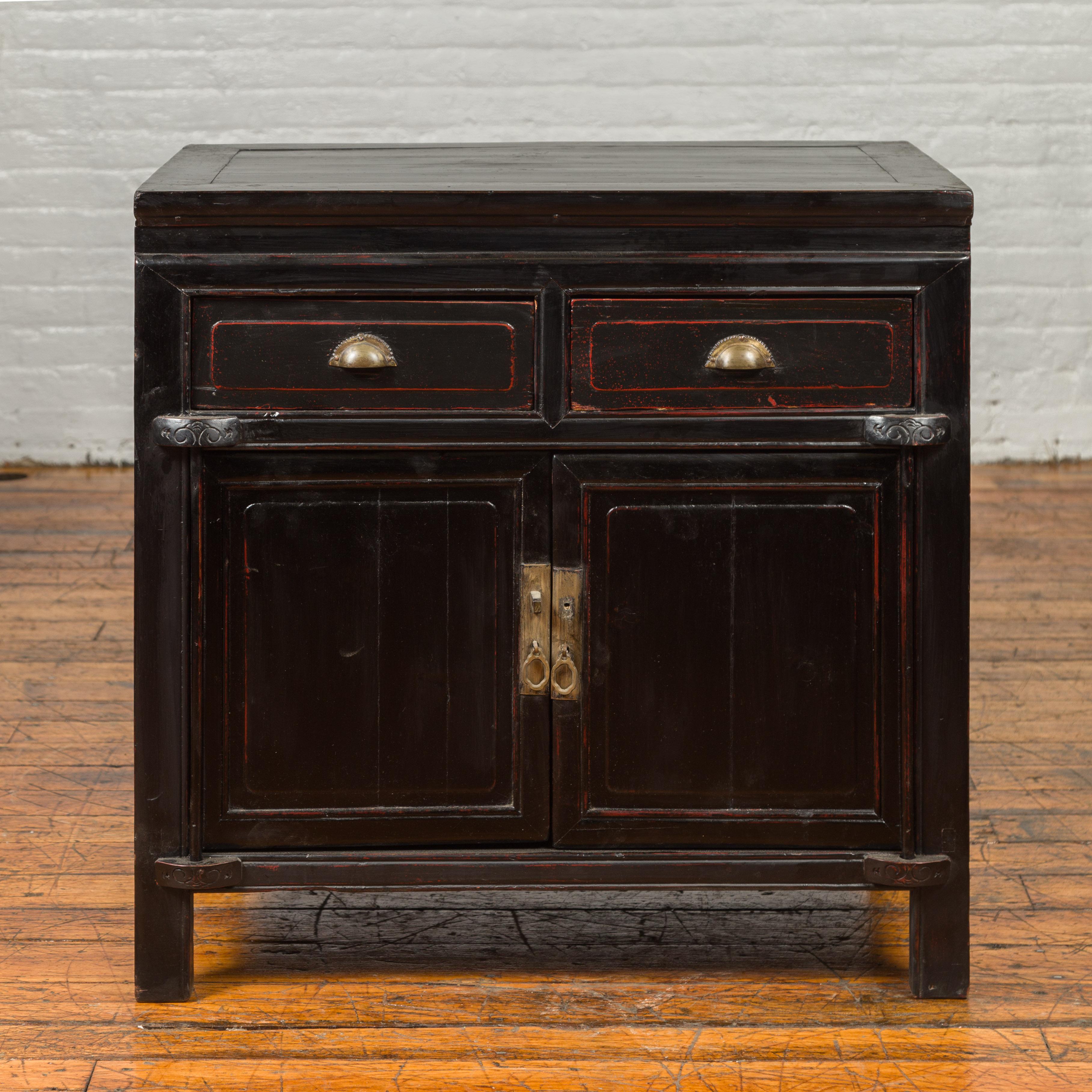 A Chinese vintage black lacquered buffet from the mid-20th century, with red highlights, two drawers and two doors. Crafted in China during the midcentury period, this small buffet captures our attention with its pure lines and dark patina. A