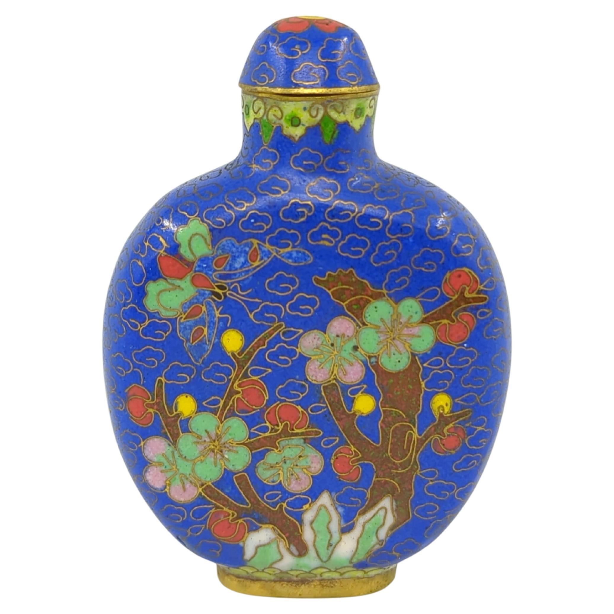 Flacon à priser vintage en cloisonne chinois sur fond bleu saphir royal, décoré d'une scène d'arbre en fleurs coloré et d'un papillon multicolore de chaque côté, d'une bordure de feuilles de ruyi sous le bord, reposant sur un anneau de pied en