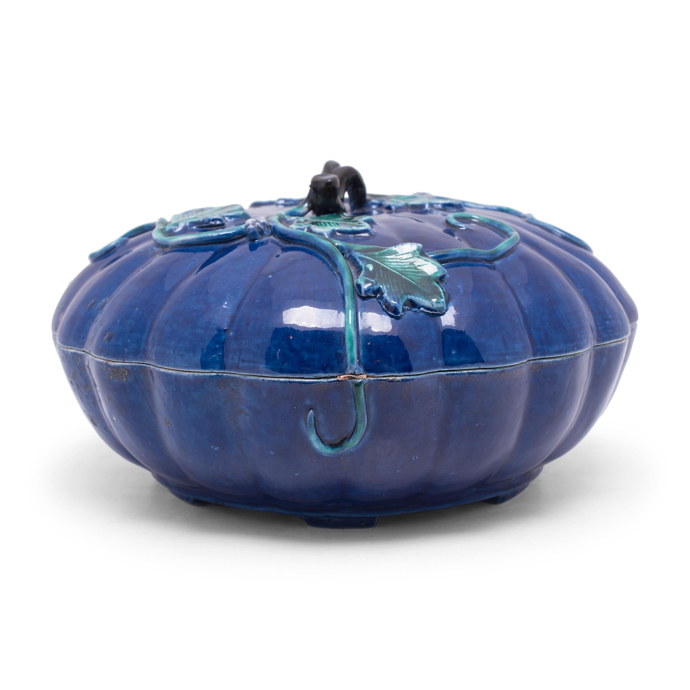 With ribbed sides and a vine-like handle, this porcelain trinket box resembles a squash or gourd, a common symbol for abundance, longevity, and a large, happy family. A royal blue glaze coats the exterior, accented by a contrasting turquoise glaze