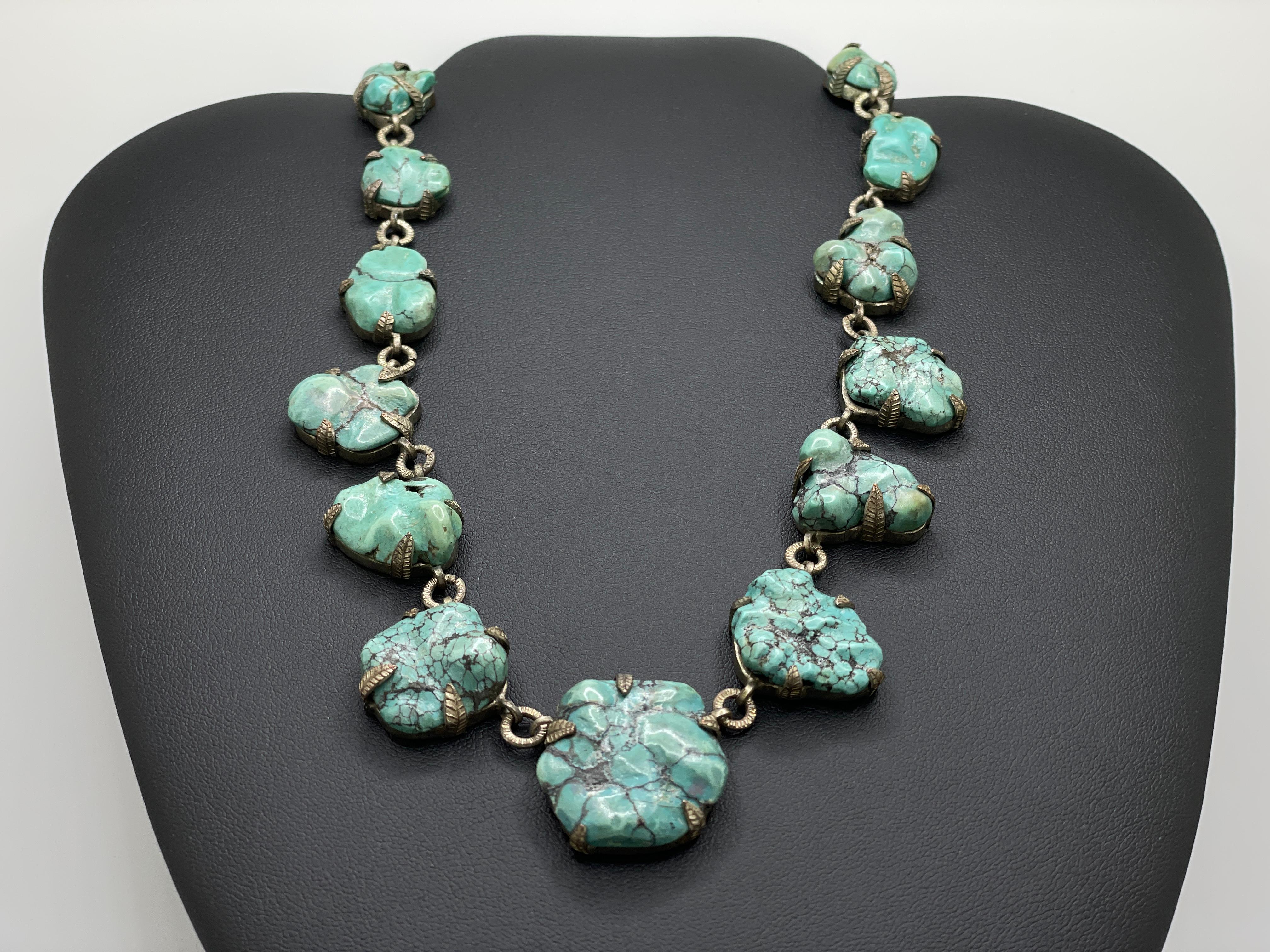 An original handmade antique sterling silver and graduated turquoise necklace. Mounted with a total of 17 natural blue/green turquoise cabochons, each individually mounted on a silver setting with intricate silver leaf-design prongs. 

Marked 