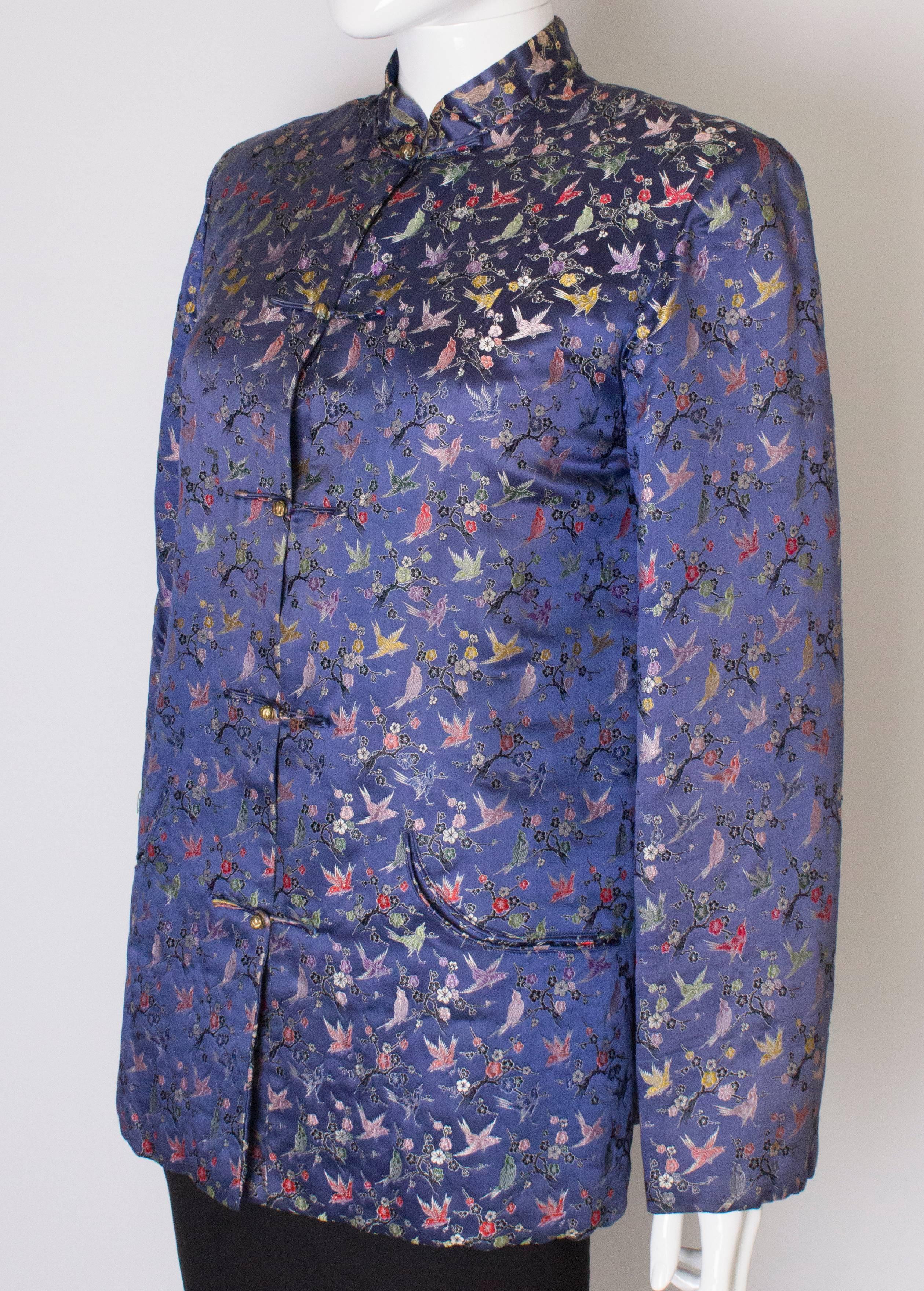 A pretty chinese jacket , in a blue /lilac coloured silk with bird and tree embroidery. It has central toggle fastenings and interesting curved pockets. The jacket has a quilted lining and a slit on either side.