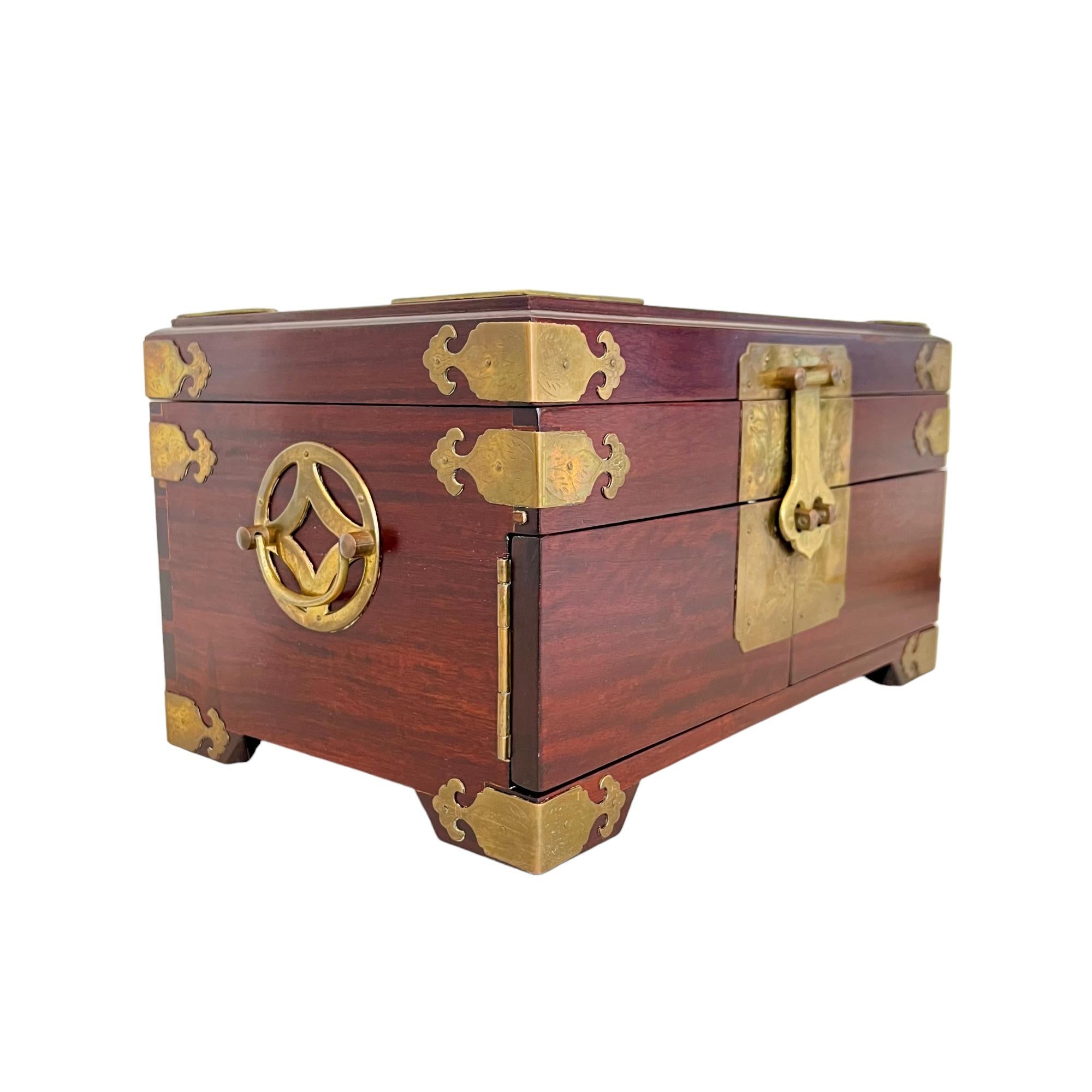 A vintage George Zee Chinese jewelry storage box. This beautifully crafted chest is constructed of wood and adorned with brass accents including a Chinese 'blessing'' character on top, chased corner braces and latch plate, and medallion style side