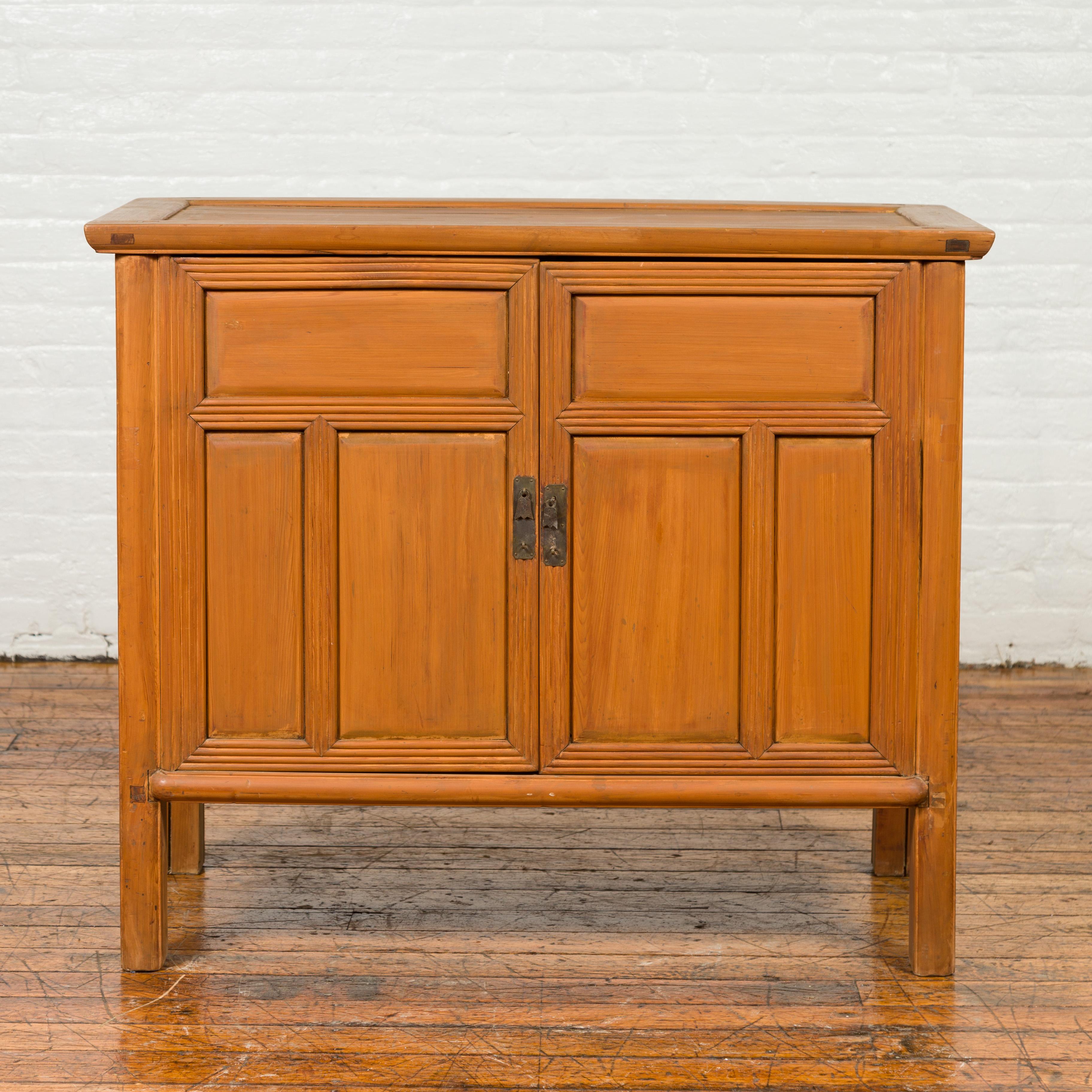 A vintage Chinese buffet from the mid-20th century, with paneled doors and hidden drawers. Discover the rustic charm of this mid-century Chinese buffet, an example of Asian craftsmanship boasting paneled doors and hidden drawers. Crafted during the
