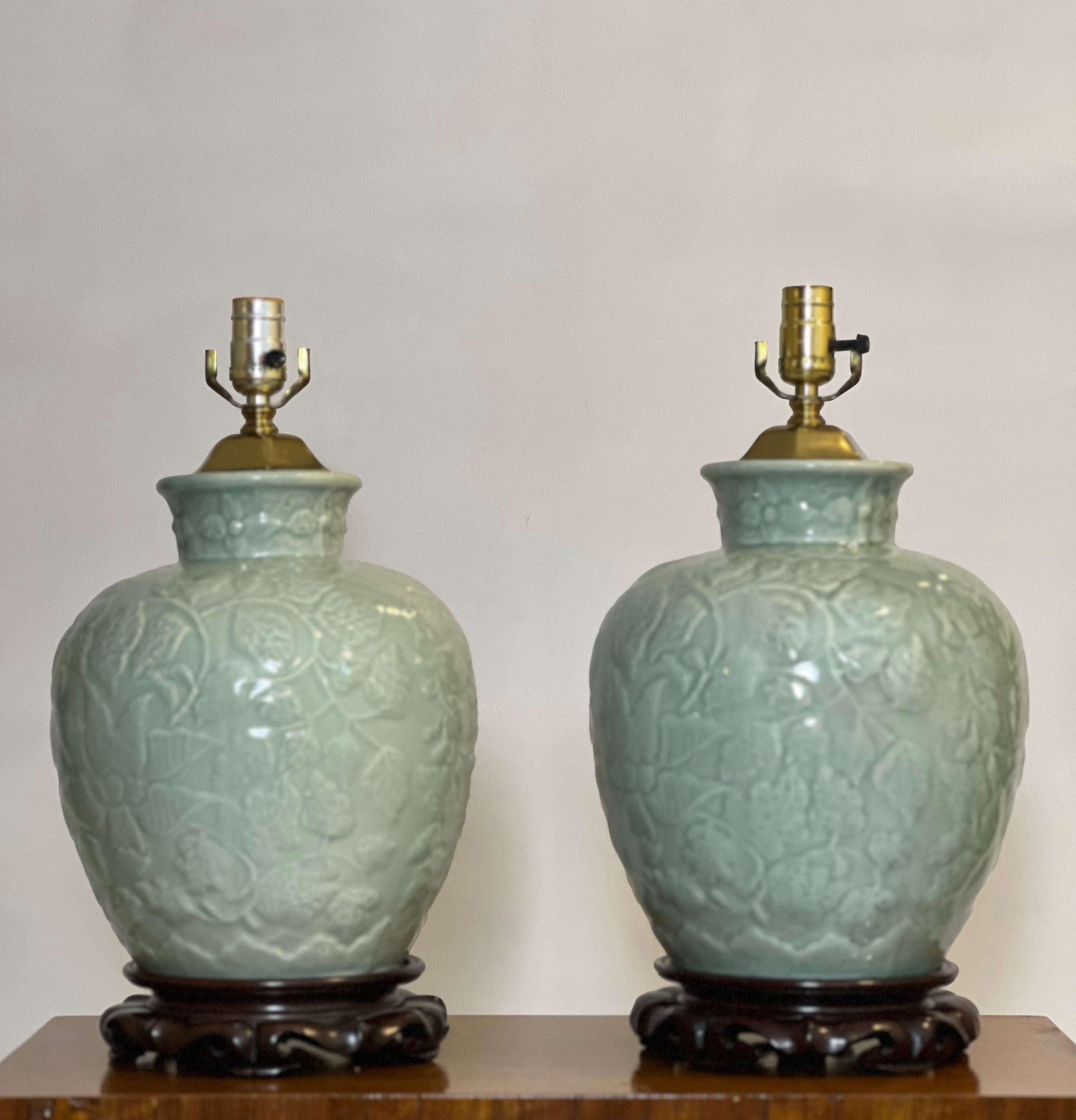 Pair of mid 20th century Chinese Celadon ginger jar style table lamps.

Gorgeous lamps in a finely crackled glaze with a raised floral and foliate design. They are set upon carved hardwood bases and have beautifully shaped, shiny brass adornments at