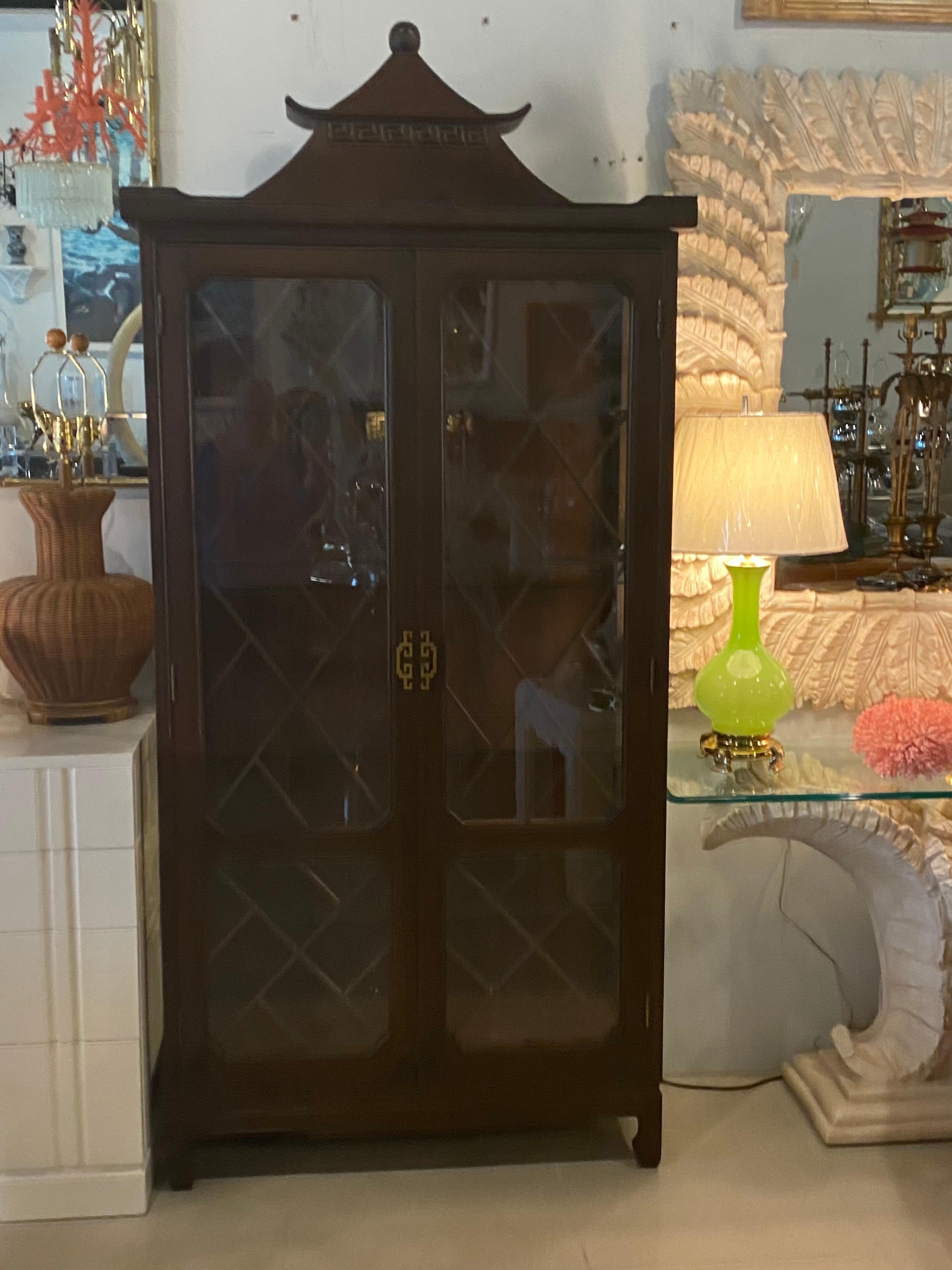 Lovely vintage pagoda top with Greek key motif. Glass doors with Chinese Chippendale wood fret design on doors. Brass detailed pulls. 4 Newly cut adjustable glass shelves. Lights up on top. Original wood finish.