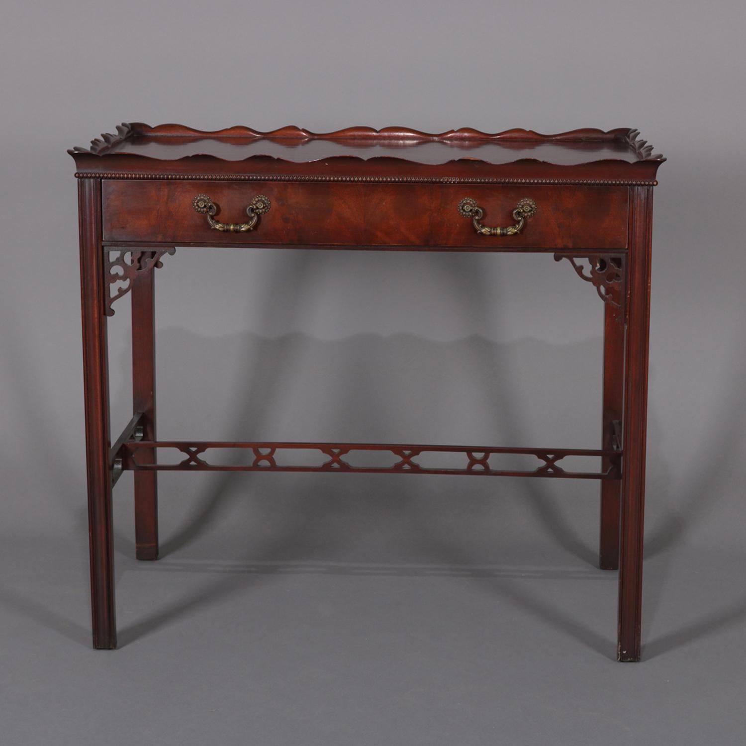 A vintage Chinese Chippendale lamp table features flame mahogany construction with top having scalloped edge surmounting single drawer cabinet raised on straight legs having pierced cutout corbels and stretcher, circa 1940.

Measures: 29