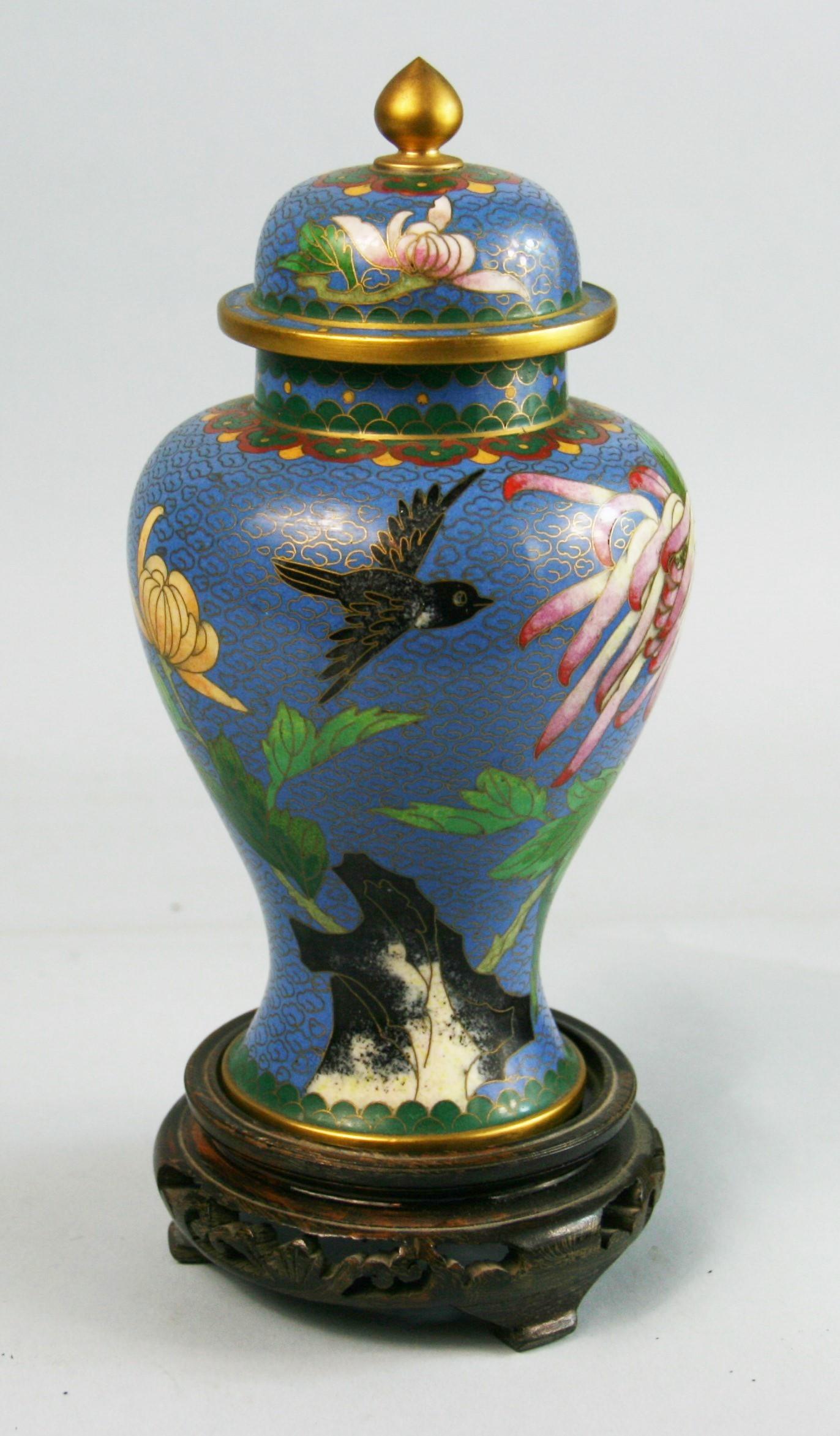 3-675 Cloisonne covered urn with birds and flower details set on a carved wood vase.