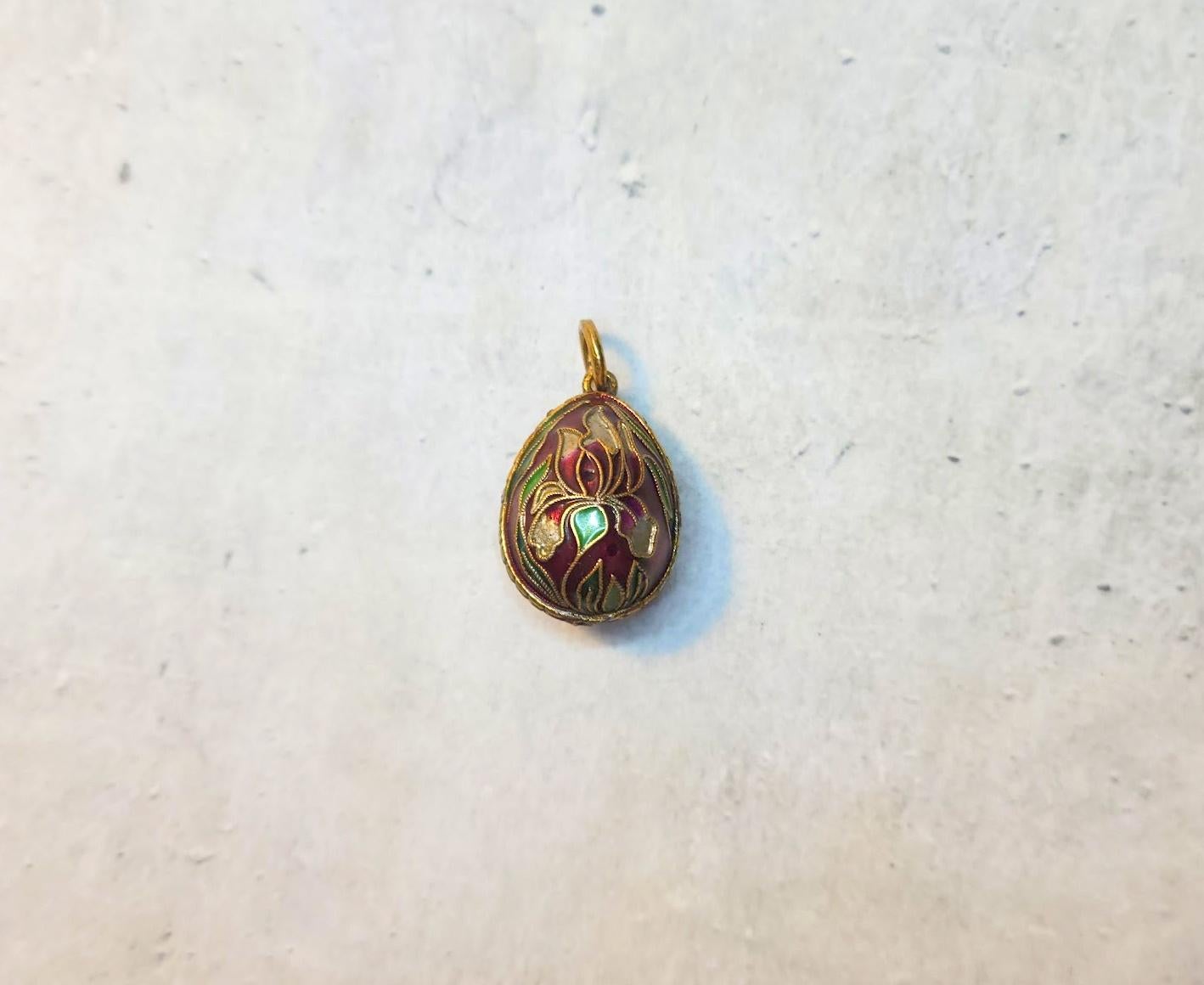 This exquisite vintage Chinese gilded silver egg pendant, adorned with stunning cloisonné enamel floral motifs and granulated accents, features the revered iris flower. In Chinese culture, the iris symbolizes the promise of good news and the arrival