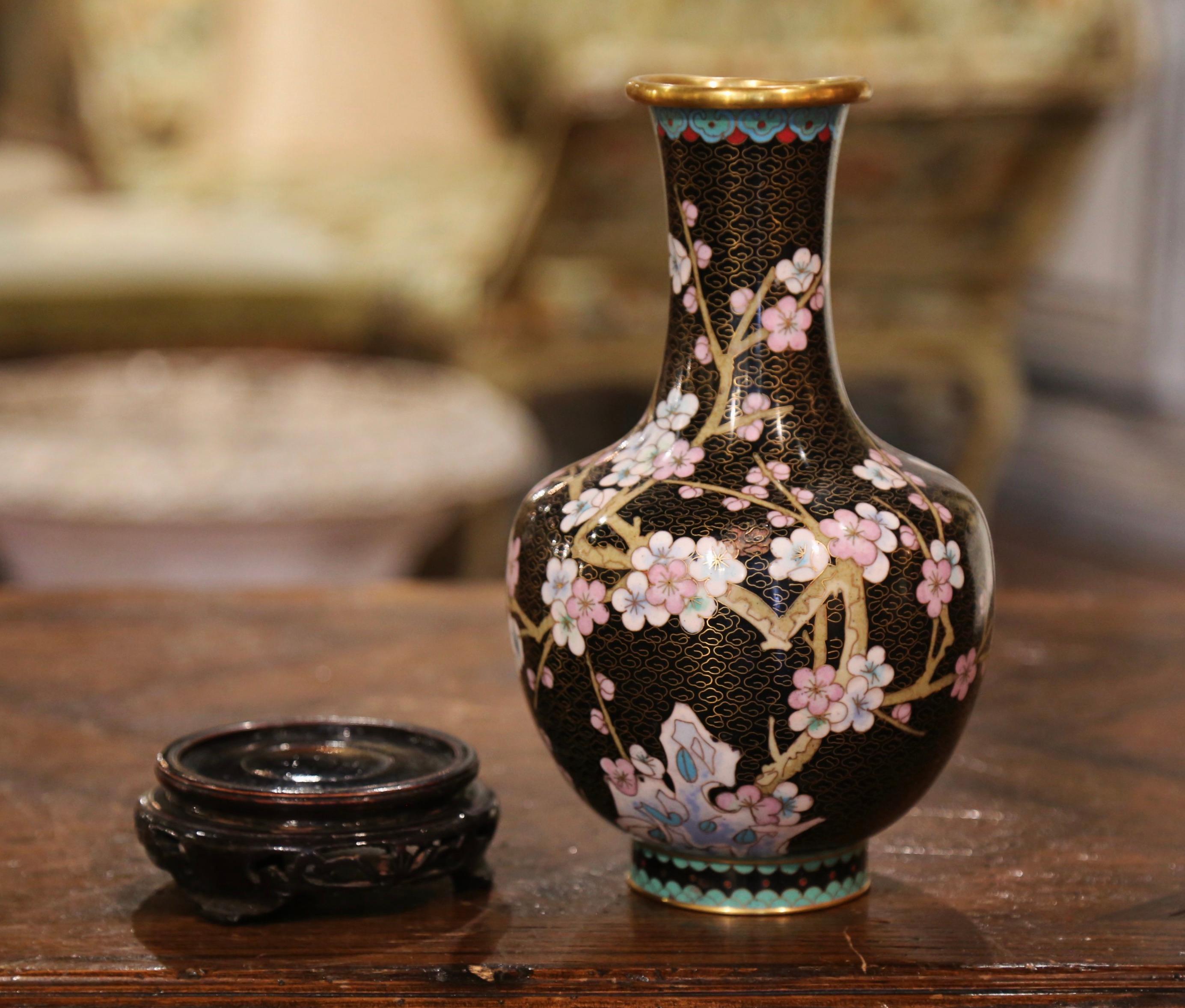 Decorate a table or a buffet with this colorful baluster vase. Created in China circa 1980, the vase sits on a carved ebonized wood stand and features floral motifs on branches in the cloisonné technique (decorative work in which enamel, glass, or