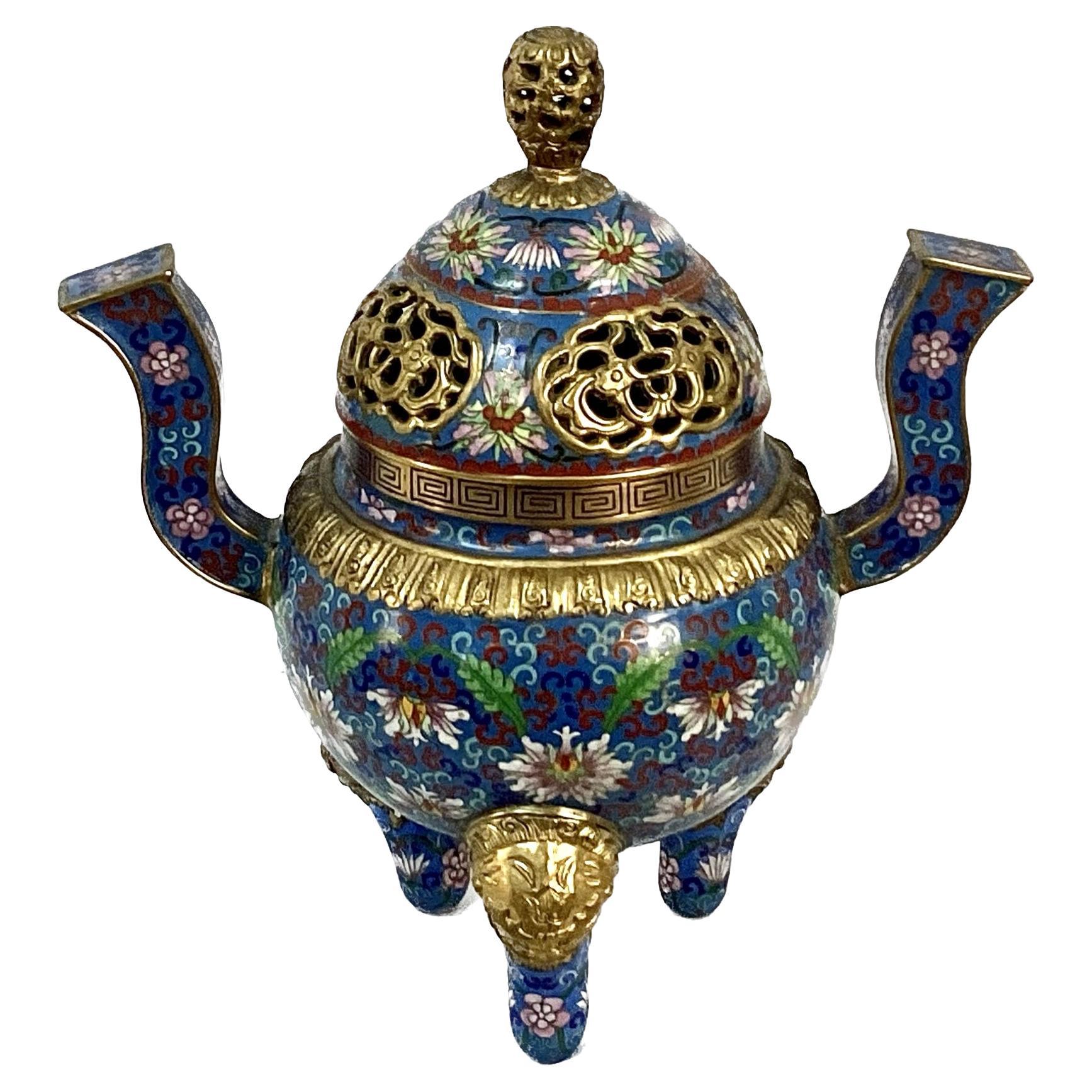 Vintage Chinese cloisonné' enamel tripod incense burner and cover. Item is raised on three legs, each covered with lion mask. Beautiful lotus scroll in colors of rich blues, pinks, whites, and greens. Inside is solid turquoise. Brass finial on top