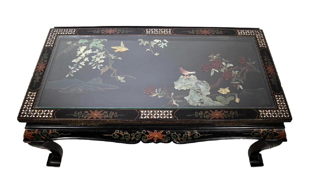 This Chinese coffee table is a precious table realized in the early to mid-20th century.

The table is on curved legs, black lacquered ebany wood, floral painted and decorated with mother of pearl inlays, a relief image made of jade and other