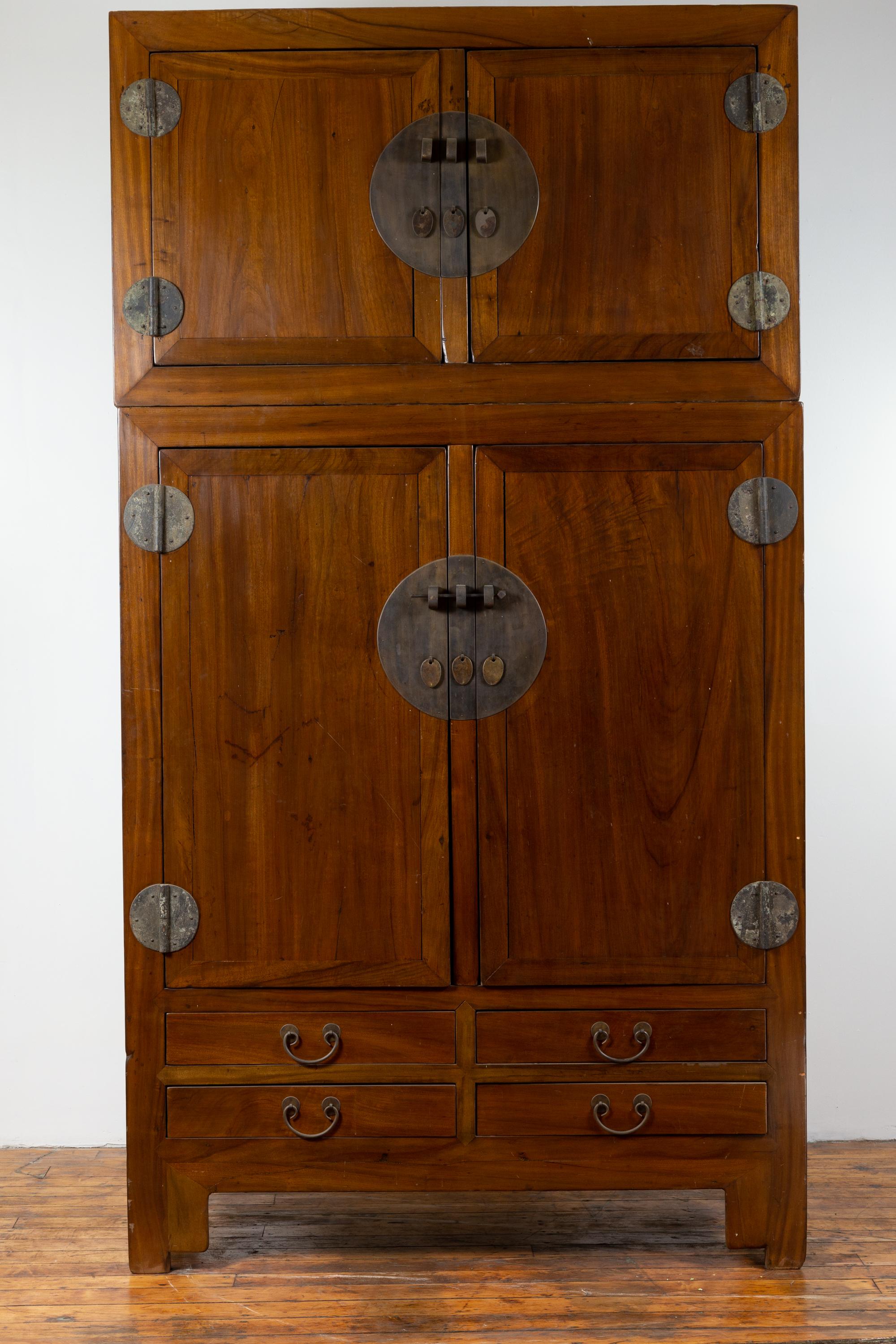 A Chinese vintage elmwood compound wedding wardrobe in two parts, with two sets of double doors, lower drawers and metal hinges. Born in China during the mid-20th century, this large elm compound wardrobe features a small upper cabinet presenting a