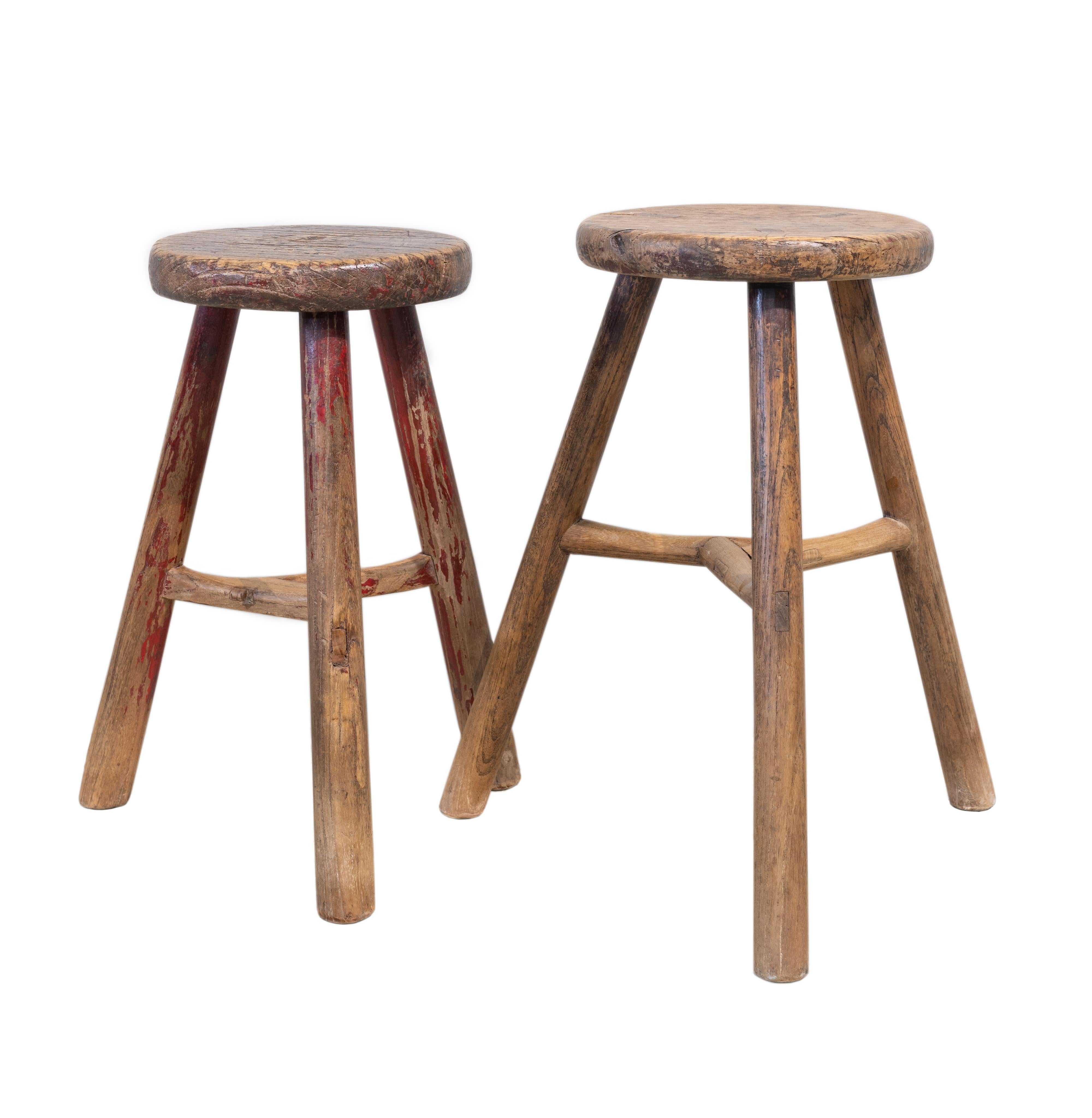 Chinese elmwood round stools with three legs from Shandong province, China. Beautifully worn with a smooth texture and very nice patina. The slightly shorter stool has some faded red paint and a nice solid 4 cm thick seat top, and the joints from